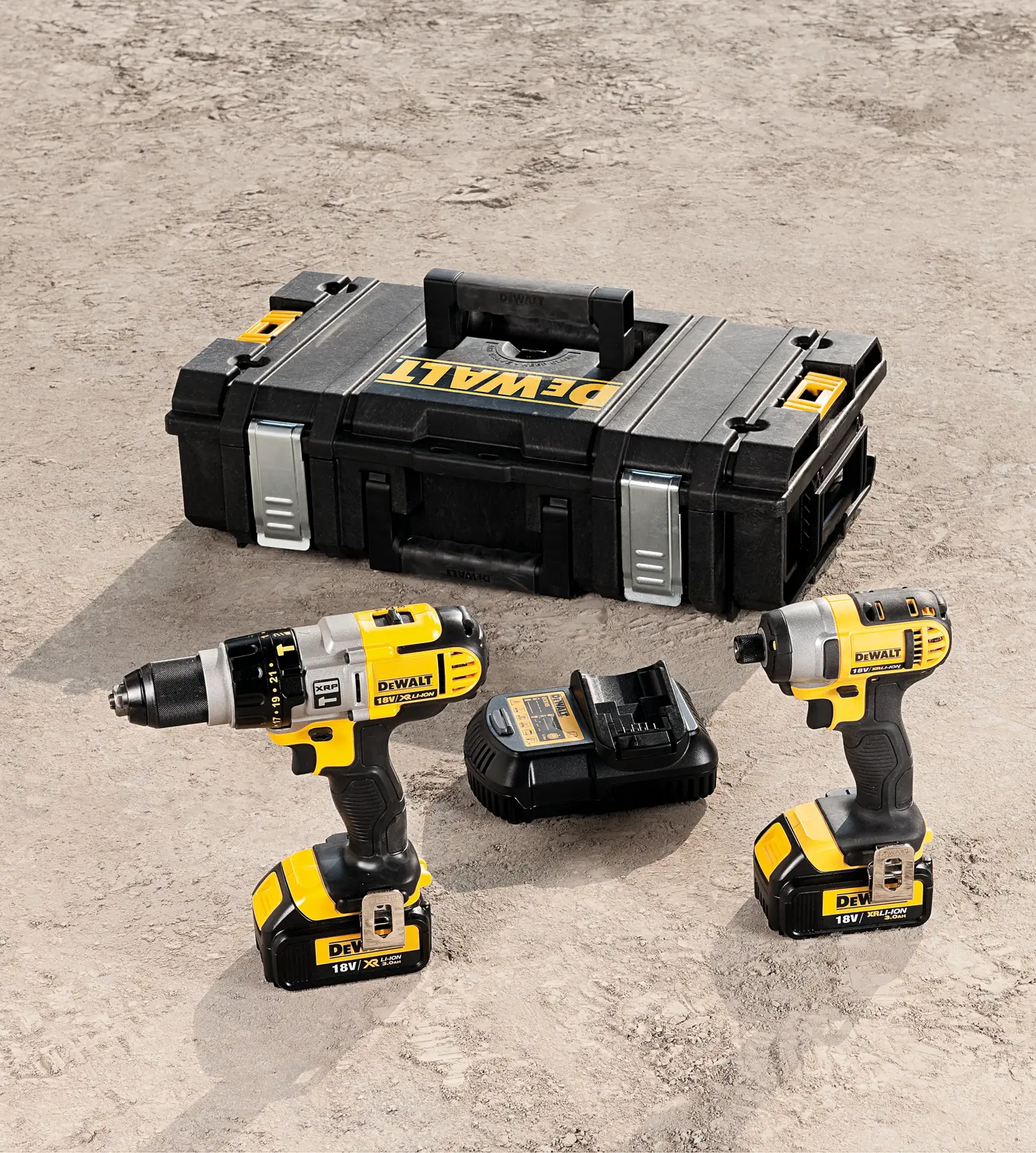A set of DEWALT power tools including a drill driver, an impact driver, a battery charger, and a sturdy black tool case placed on a concrete surface.