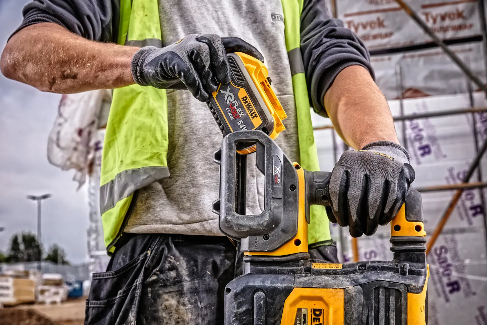 Nahaufnahme einer Person mit Handschuhen und Warnweste, die gerade einen DEWALT DCB548 XR FLEXVOLT Akku in ein passendes DEWALT Elektrowerkzeug auf einer Baustelle einsetzt.