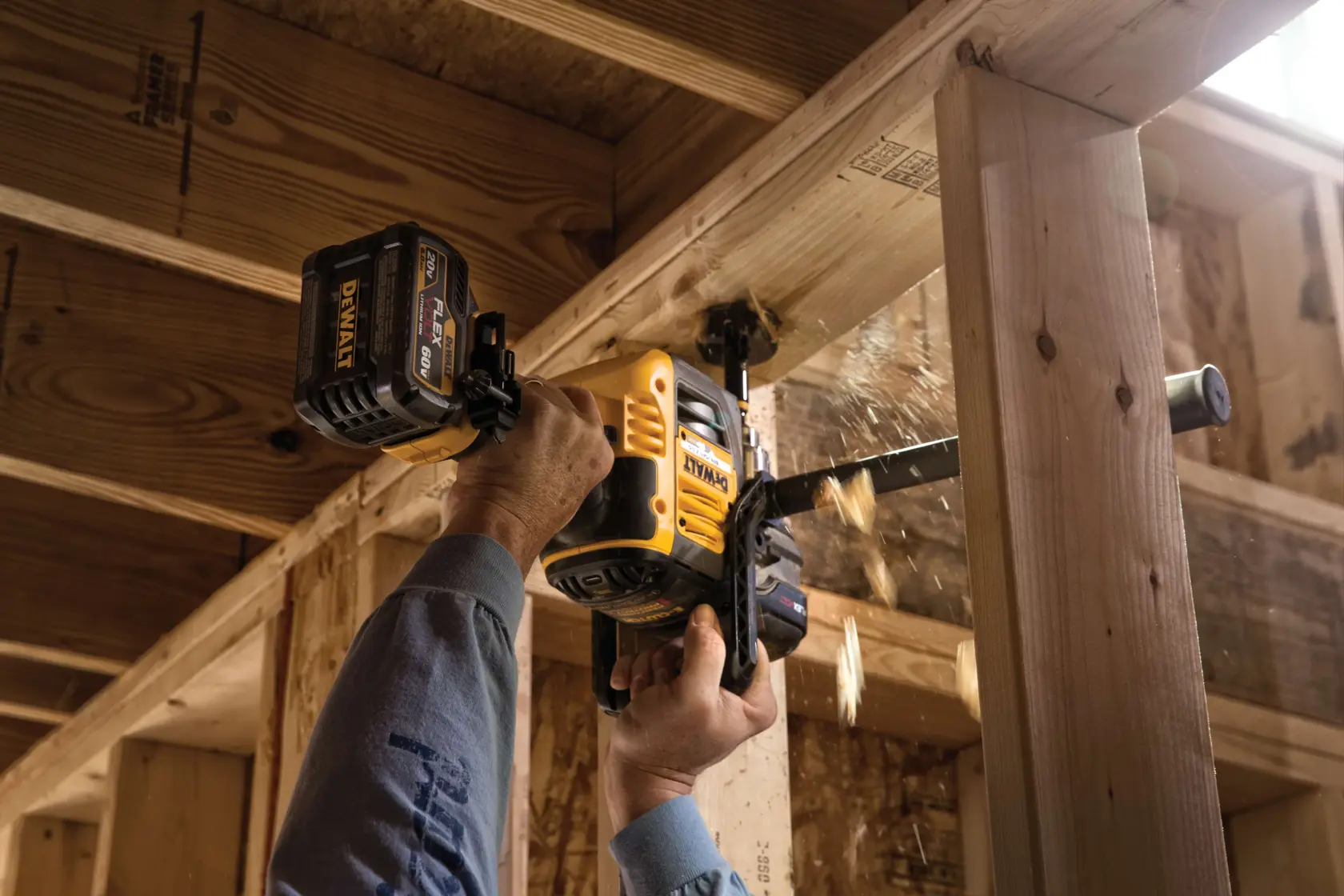 A person uses a DEWALT cordless power drill (model DCD460T2) to bore a hole through a wooden beam in a construction site.