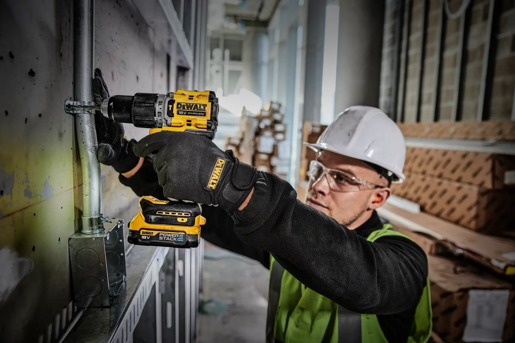 Worker uses a DEWALT DCD805E1T drill on an industrial site, wearing safety gear and gloves.