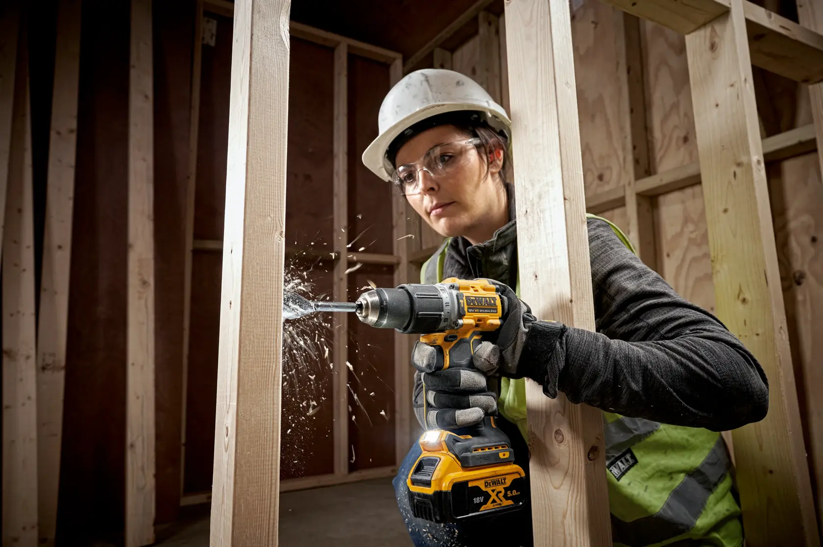 Person using a DEWALT cordless drill to create holes in wooden beams at a construction site.