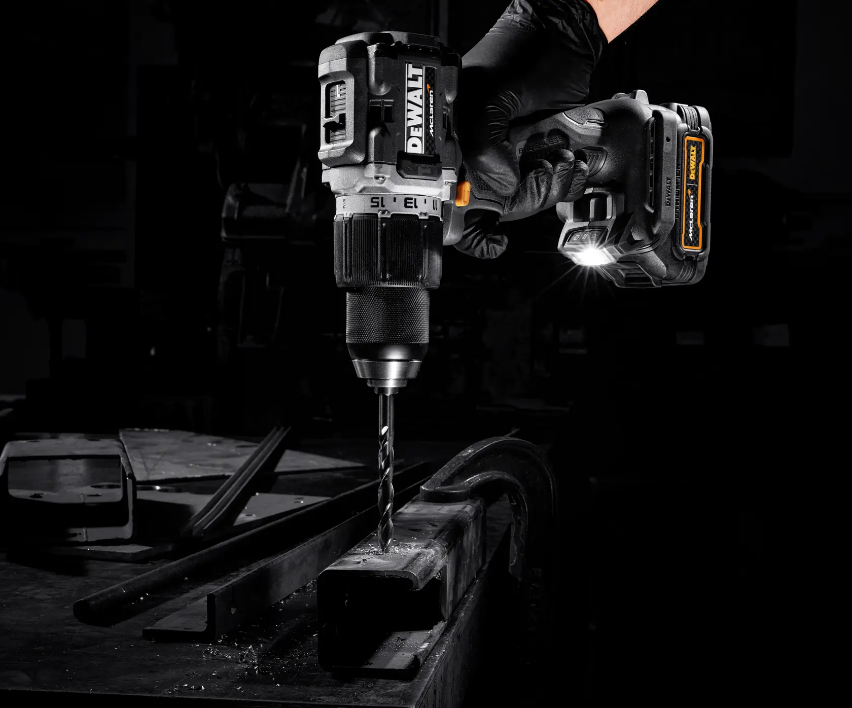 A DEWALT cordless drill with a LED light attachment being used to drill into a piece of metal by a gloved hand in a workshop setting.