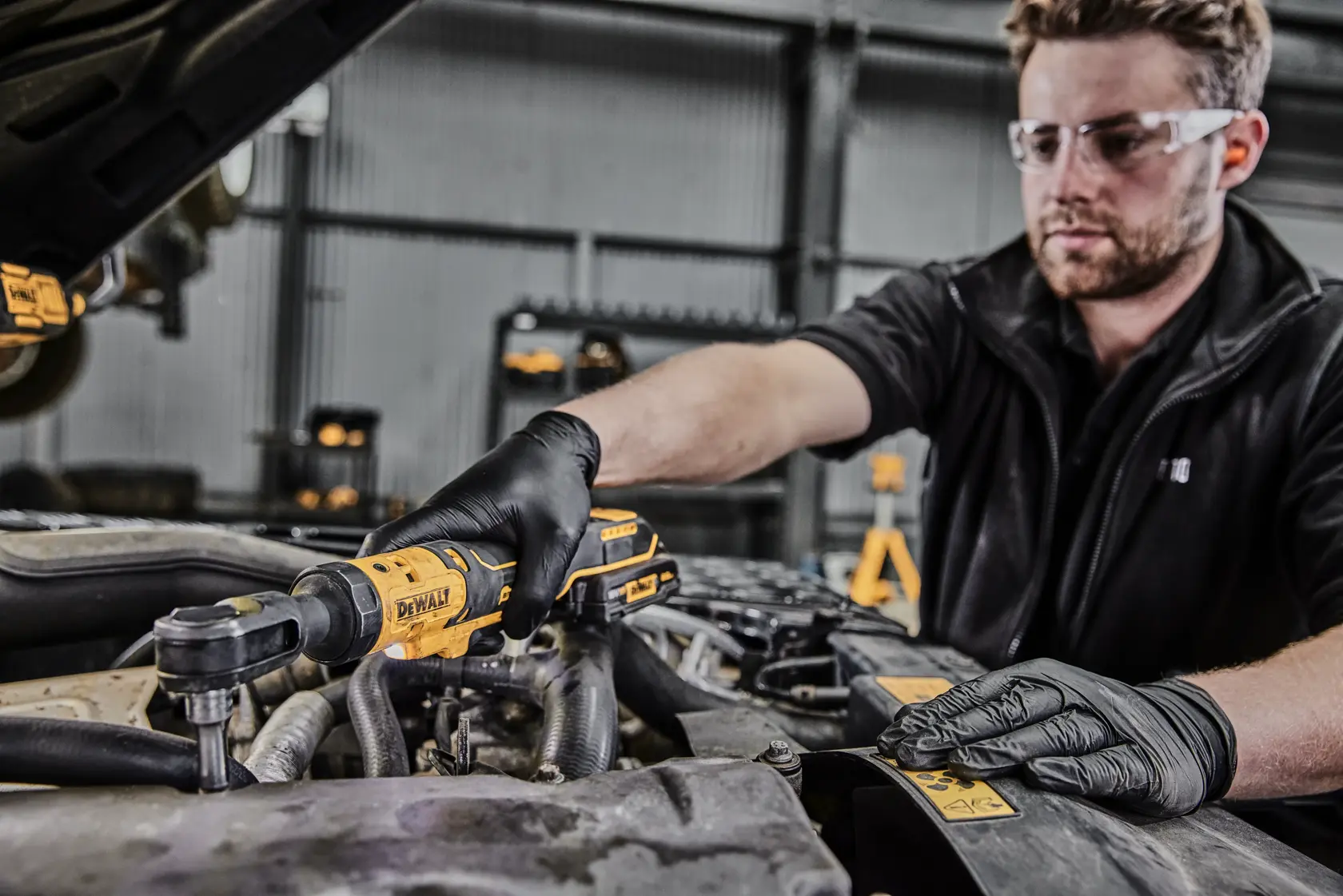 Eine Person mit schwarzen Handschuhen verwendet ein DEWALT Akku-Ratschwerkzeug (DCF513N), um an einem Auto-Motor in einer