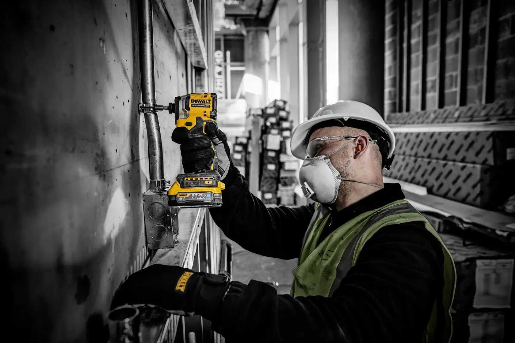 Worker uses a DEWALT DCF850E2T impact driver on metal piping at a construction site, wearing gloves and safety gear.