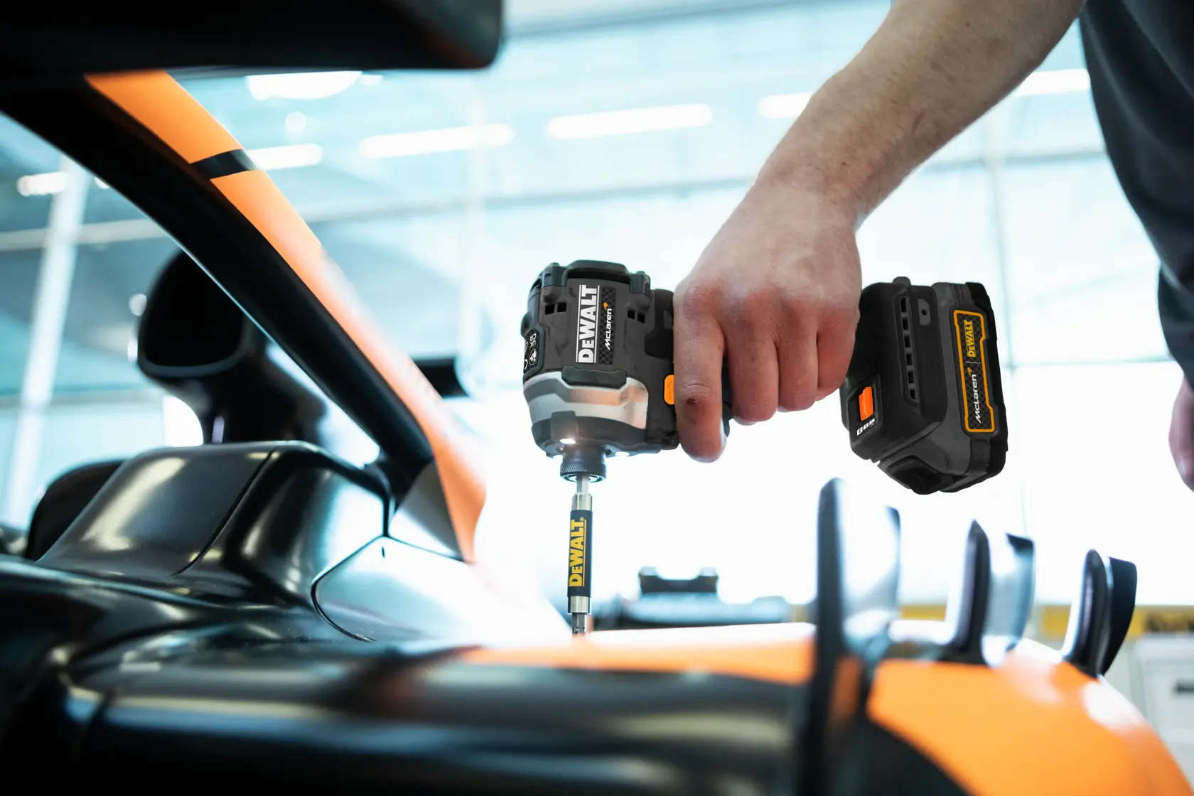 A person using a DEWALT cordless impact driver to fasten or remove a screw on a sleek, orange and black automotive component.