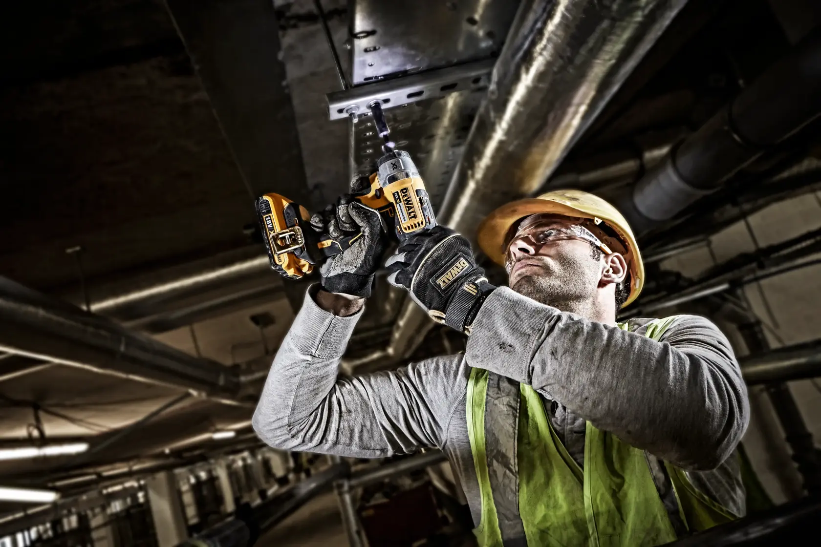 Worker uses DEWALT cordless drill DCF886N on metal ceiling. Wearing gloves, helmet, vest in an industrial setting.