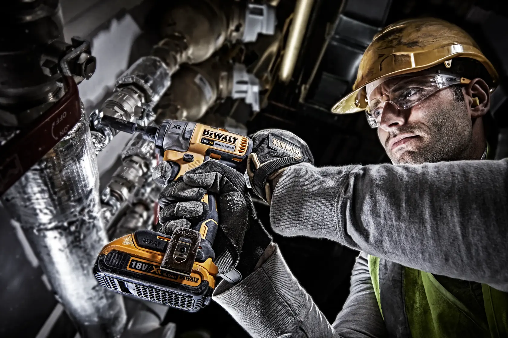 Worker uses DEWALT DCF886N cordless impact driver on pipes, wearing gloves, helmet, and safety glasses.