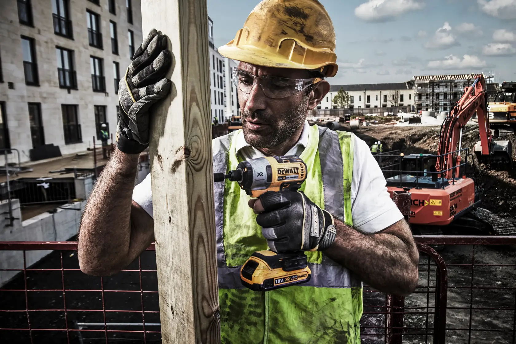 Worker using DEWALT DCF886N cordless impact driver on wood at construction site, wearing gloves and high vis vest.