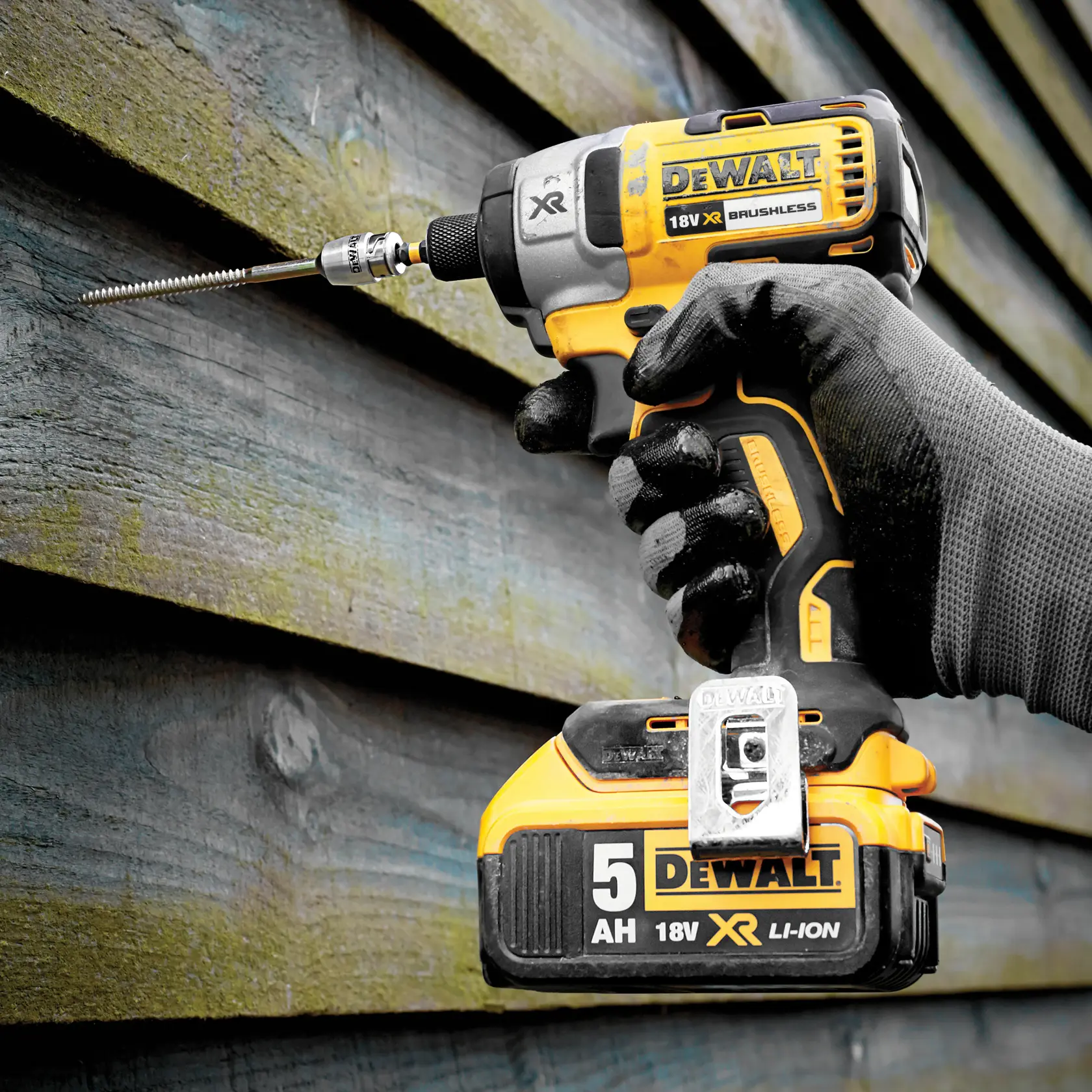 DEWALT 18V XR impact driver being used to drive a screw into a wooden wall by a gloved hand.