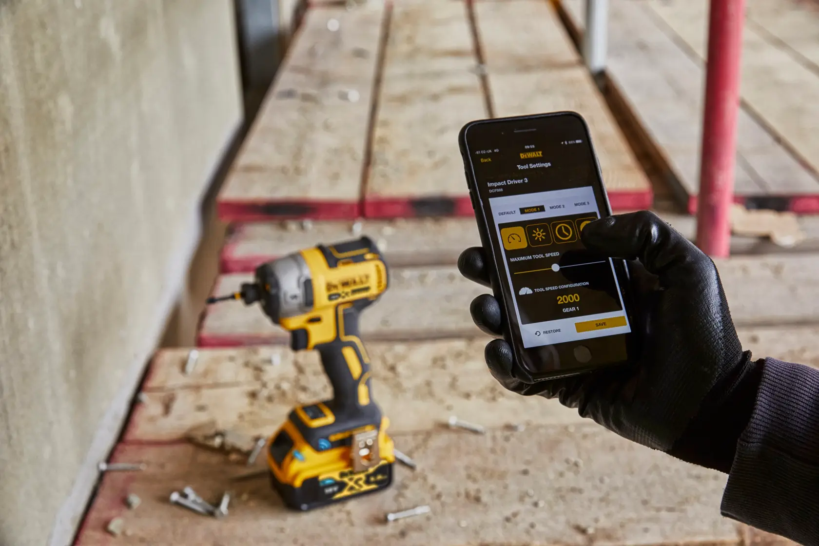 DEWALT drill on a work site next to a person adjusting settings via app on a smartphone with glove.