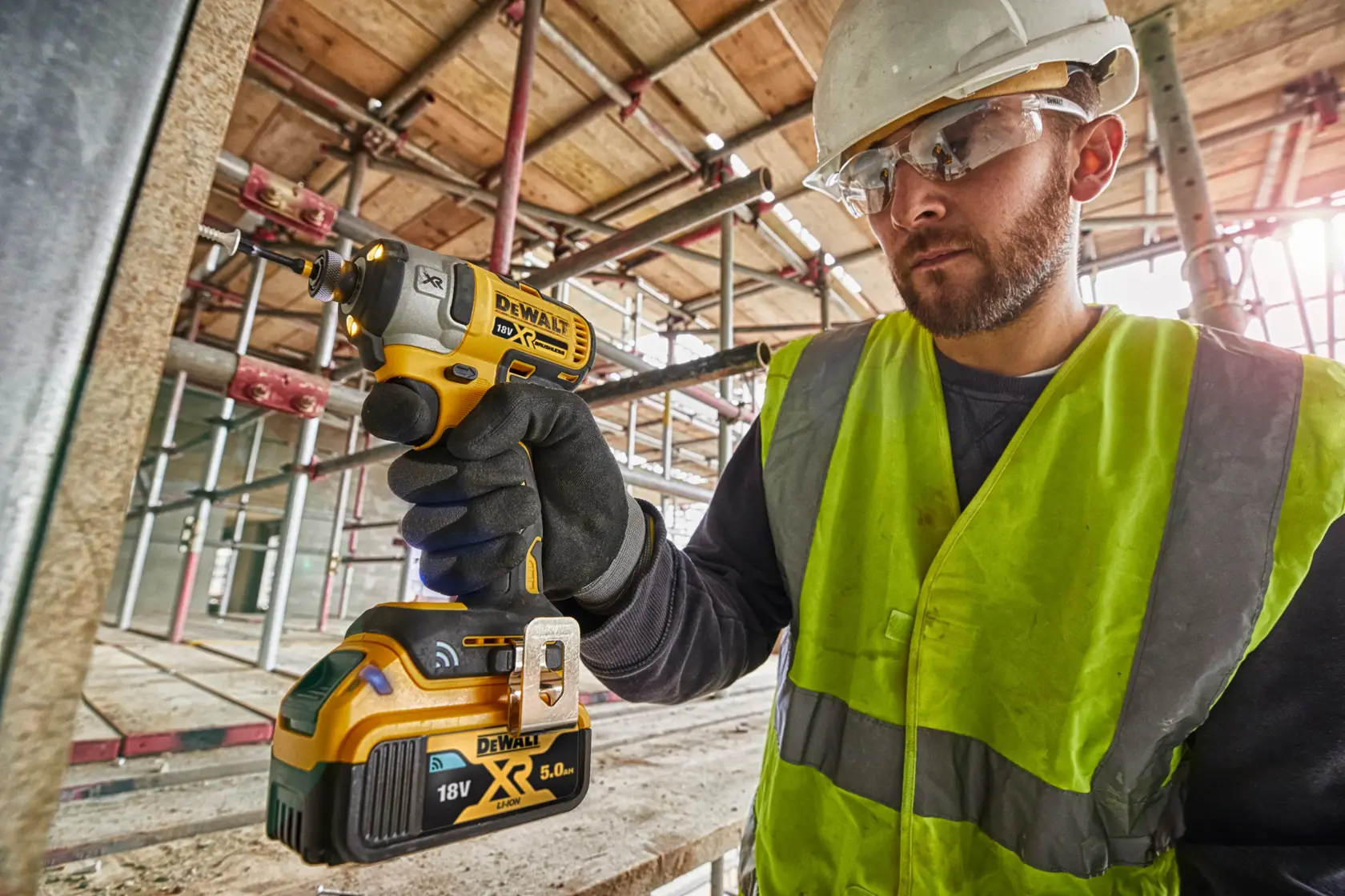 Worker uses a DEWALT DCF888D2B cordless drill at a construction site while wearing safety gear.