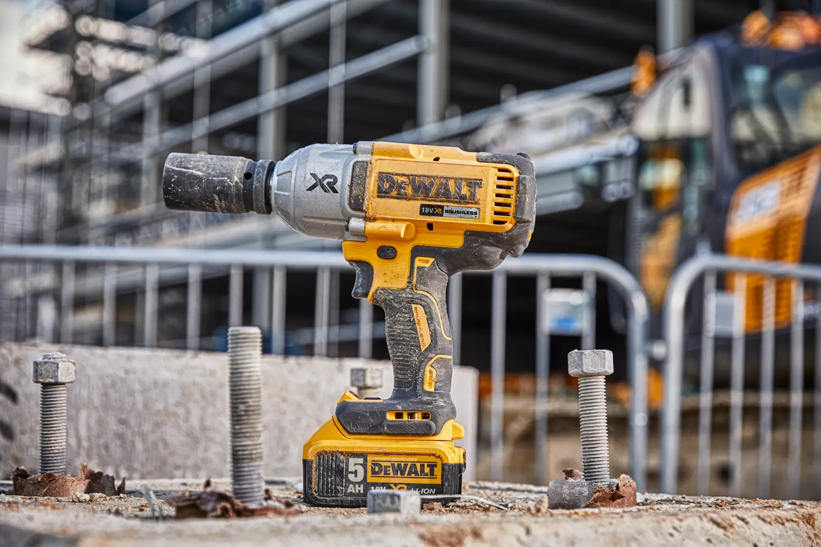 A DEWALT cordless impact wrench is shown standing upright on a construction site, surrounded by large bolts and concrete debris. Industrial equipment and a metal fence are visible in the background.