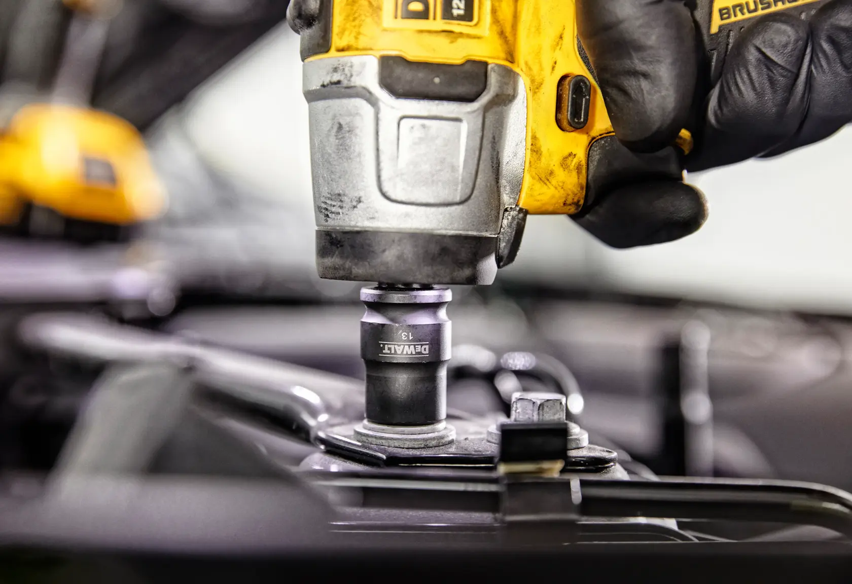 Close-up of a DEWALT cordless impact wrench being used, held by a gloved hand, tightening a bolt on a piece of metal equipment.