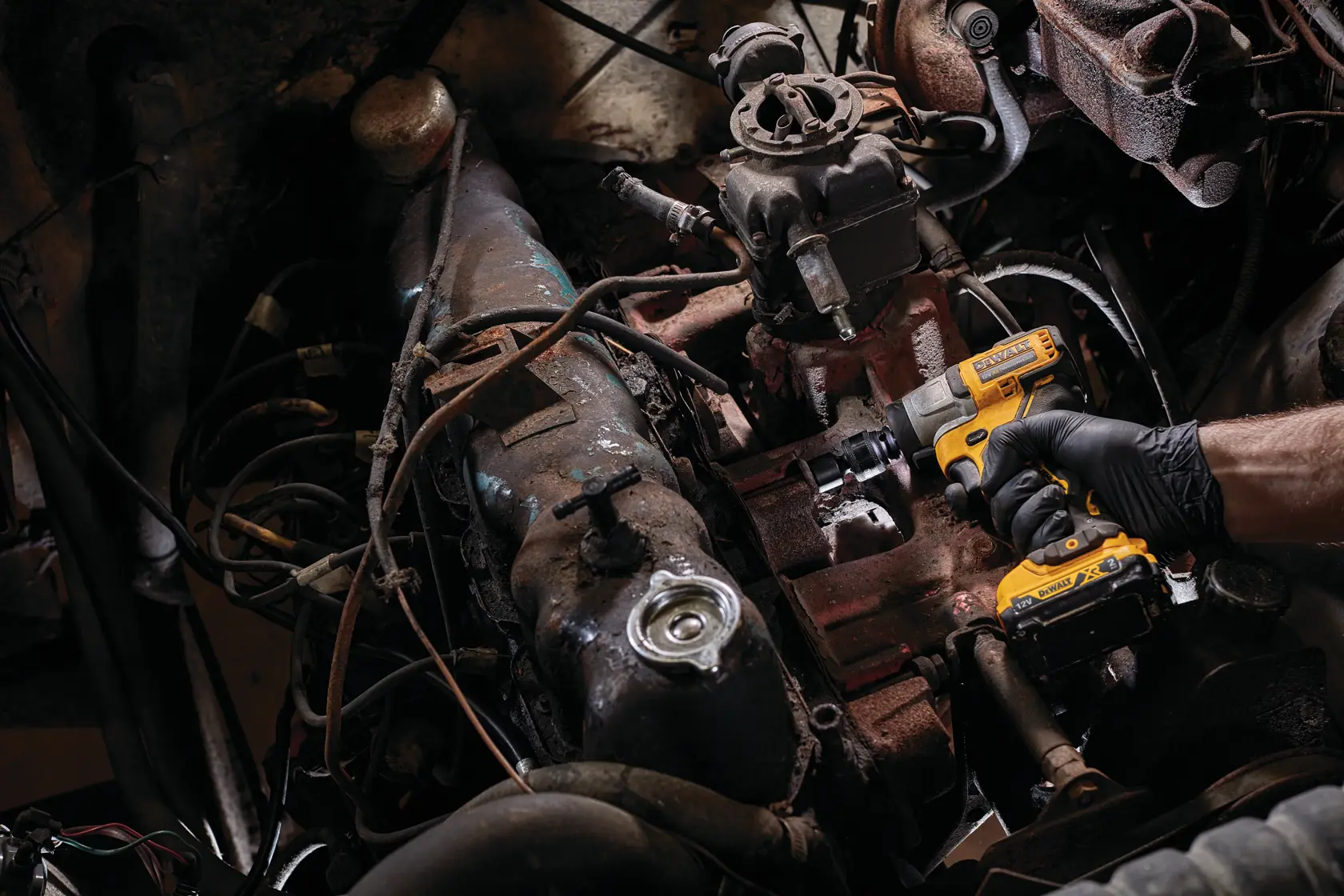 A person wearing a black glove is using a DEWALT DCF902D2 cordless impact wrench to work on an engine inside a vehicle.
