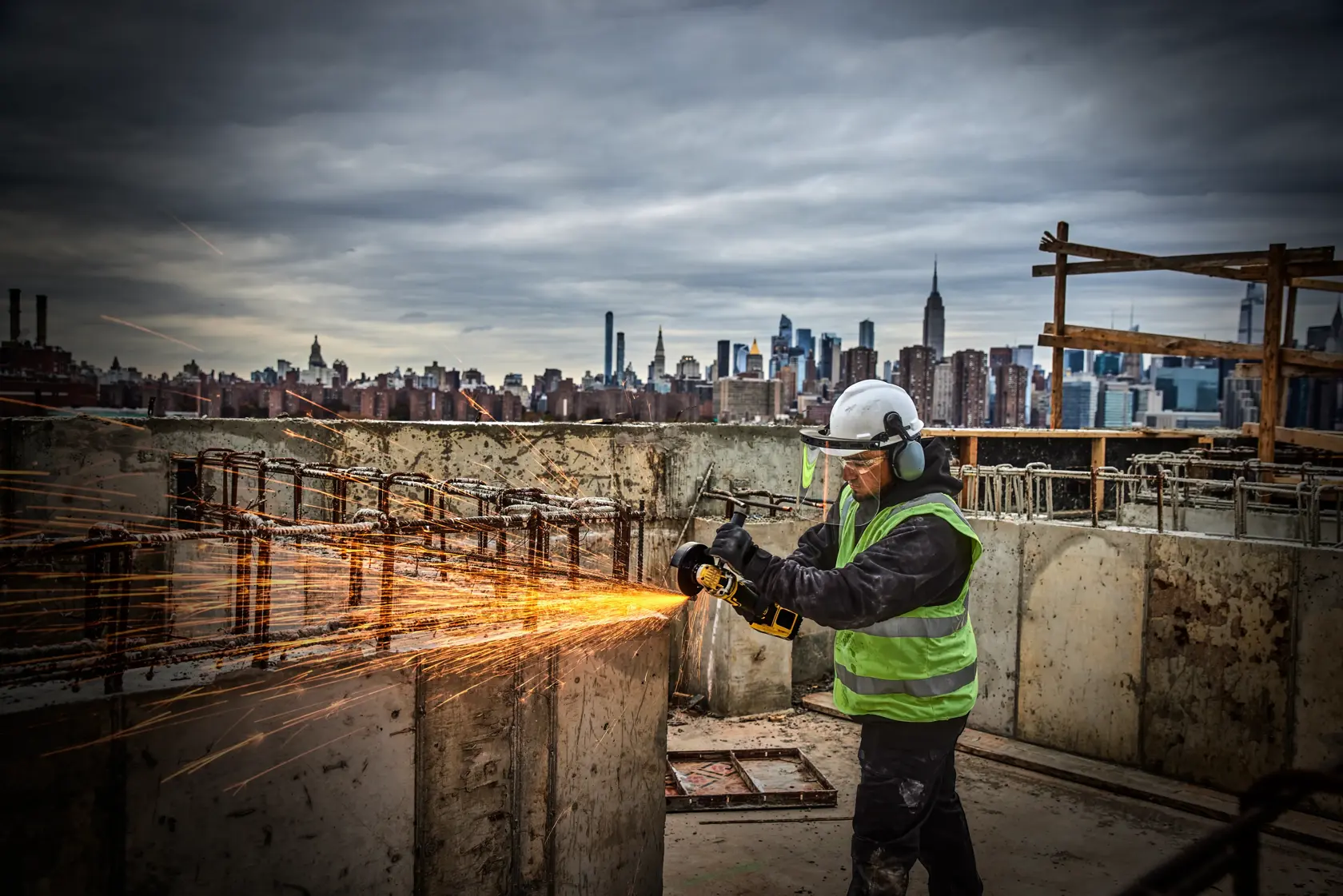 Worker using DEWALT grinder DCG405P2-IN, DCG405P2, DCG405P2-GB on site, sparks flying, city skyline in background.