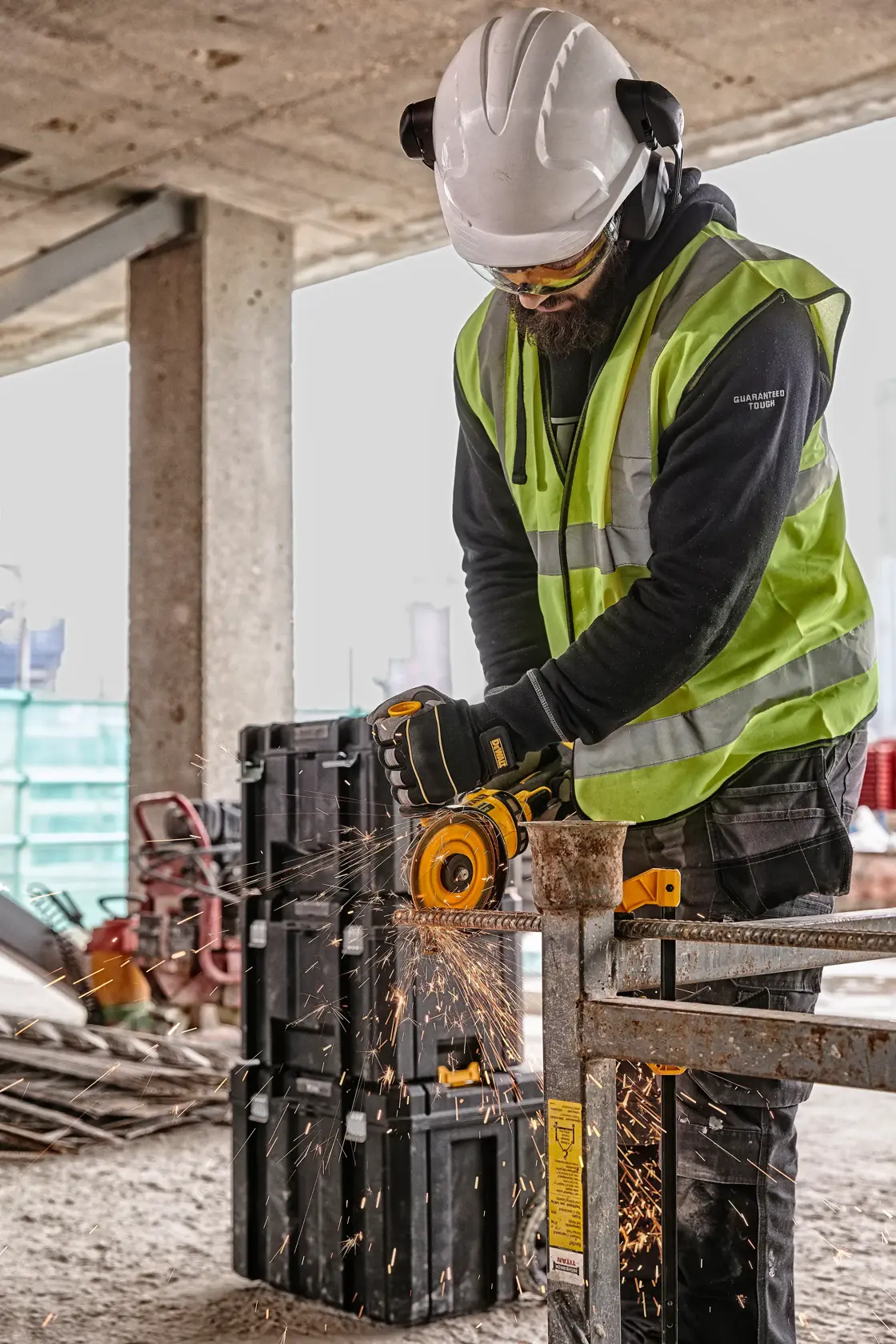 Worker uses DEWALT grinder to cut metal, wearing safety gear on a construction site. Sparks fly from the grinding.