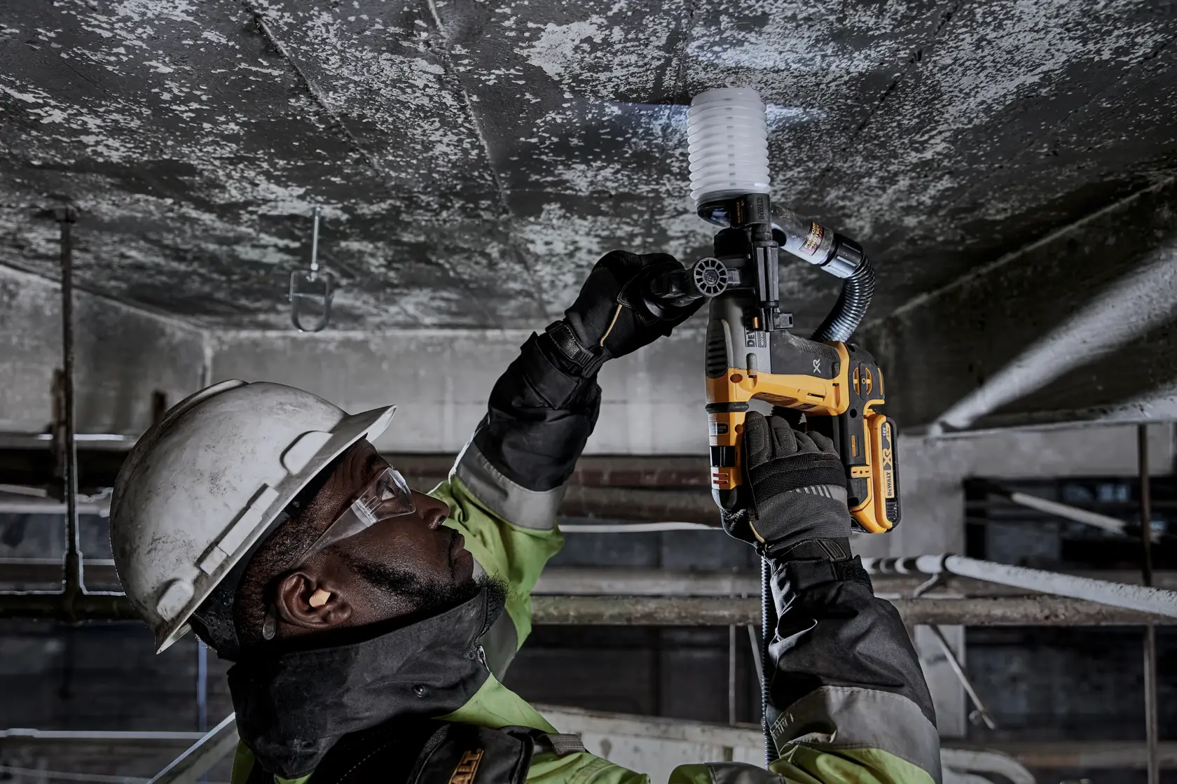 Worker uses a DEWALT DCH172D2 rotary hammer drill with dust extractor to drill into a concrete ceiling.