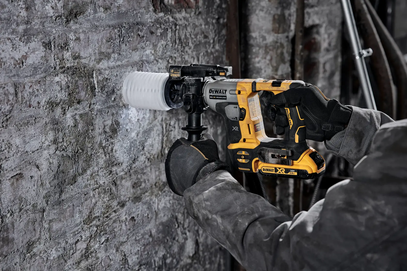 DEWALT cordless hammer drill being used on a concrete wall by a person wearing gloves and a work jacket.