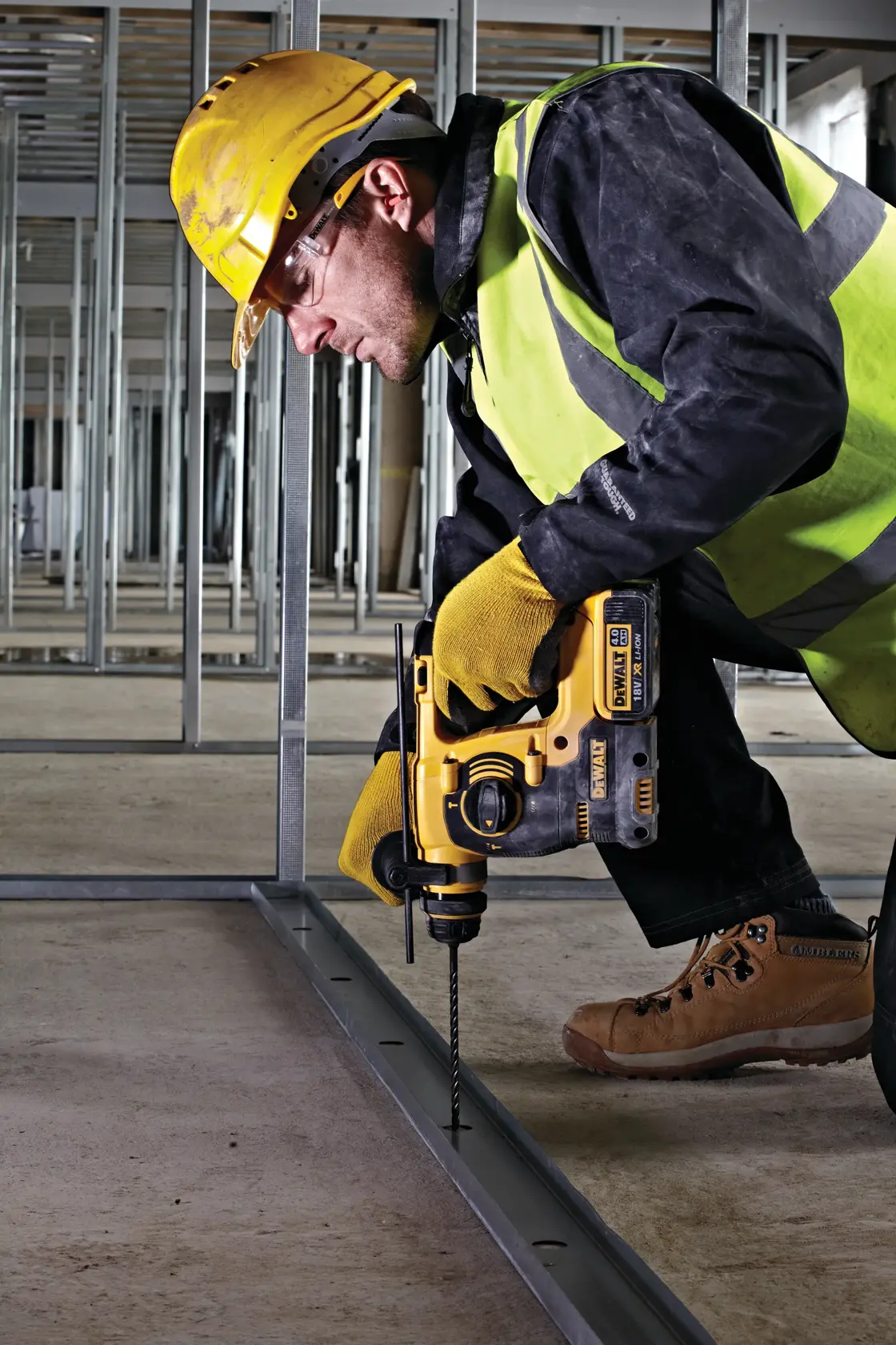 Worker drills into metal frame using a DEWALT tool, wearing safety gear at a construction site.