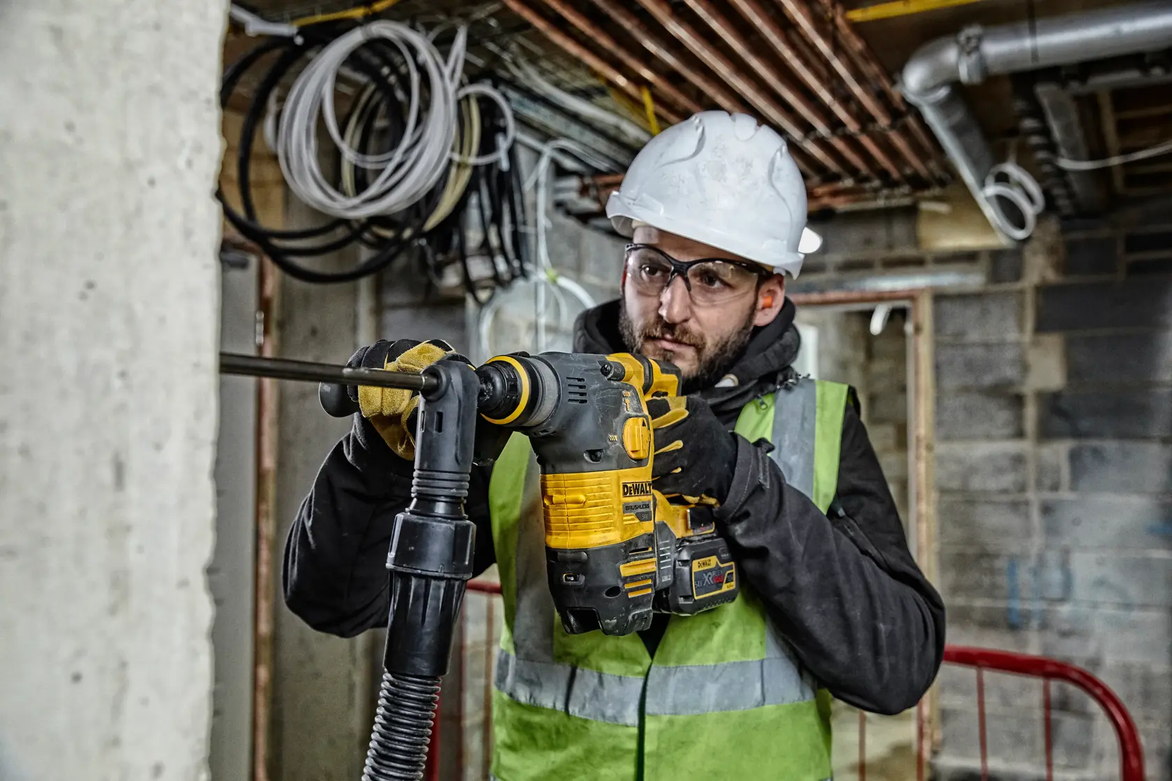 Worker using a DEWALT rotary hammer drill on concrete at a construction site, wearing safety gear.