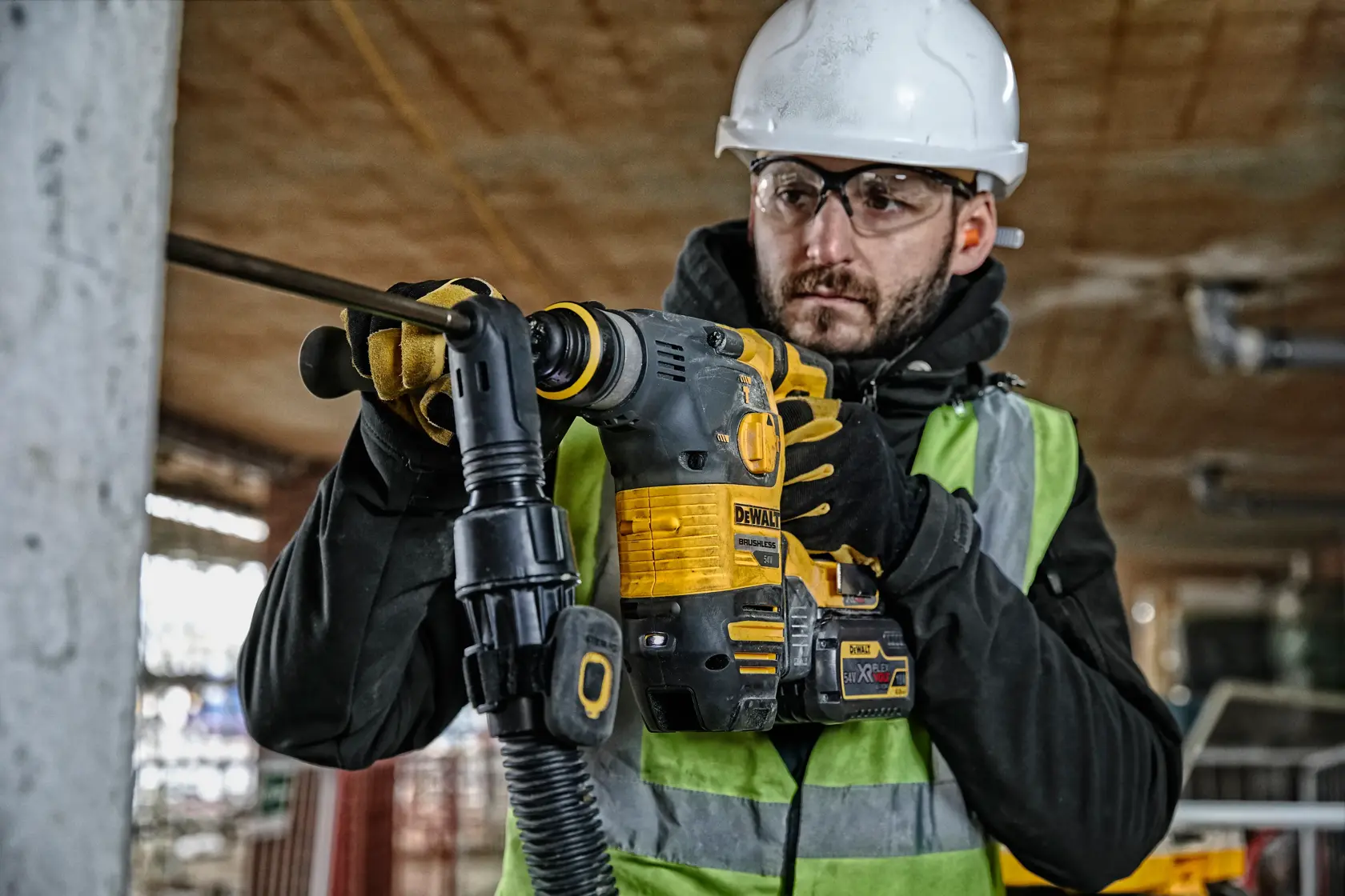 Worker using a DEWALT DCH323T2 rotary hammer drill at a construction site, wearing safety gear and gloves.