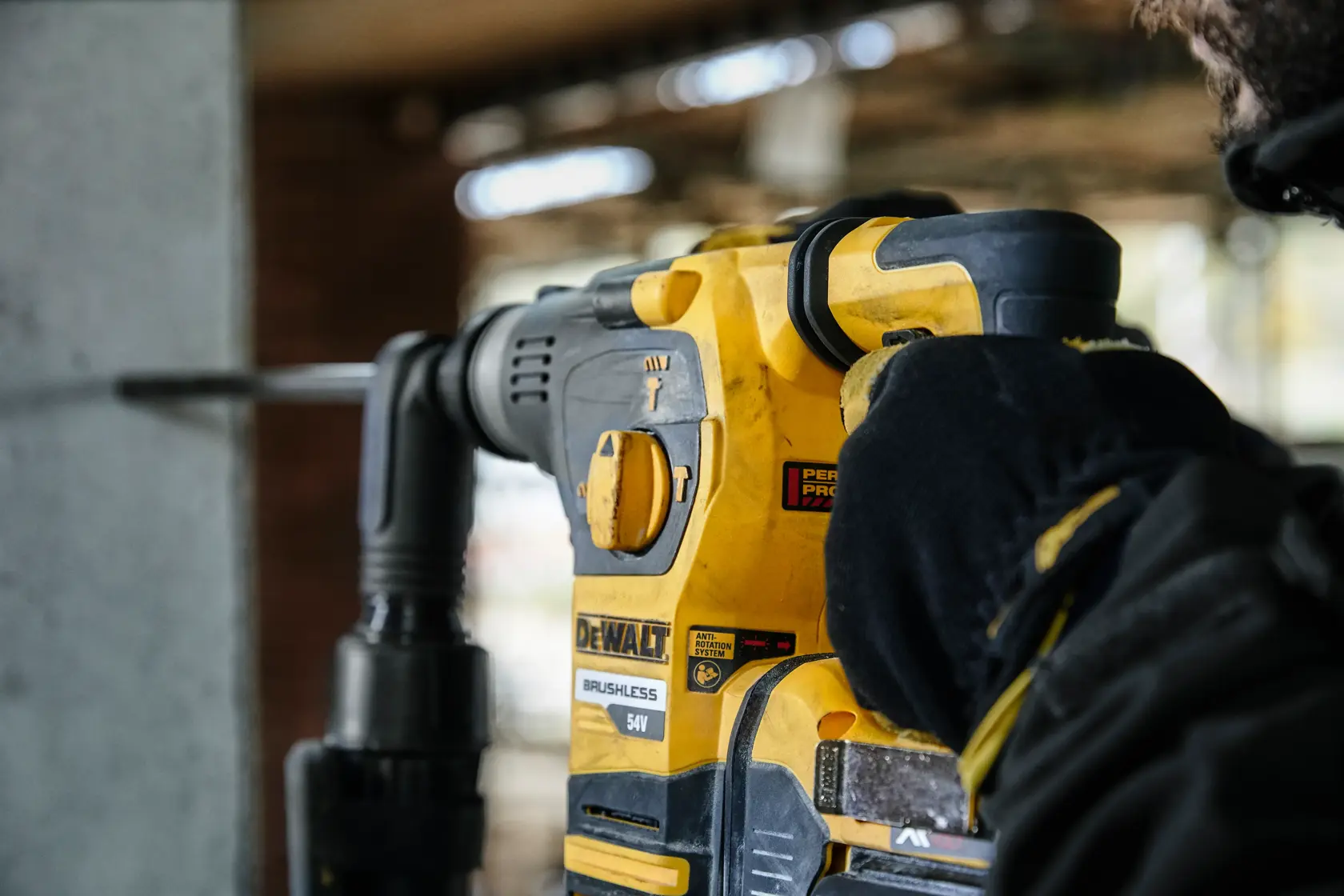 DEWALT rotary hammer drill in use, drilling into concrete. Close-up of tool and gloved hand.