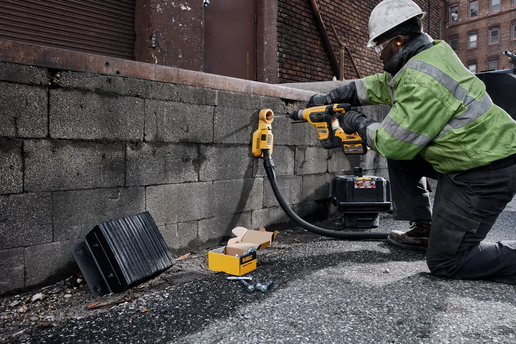 Worker uses DEWALT rotary hammer drill DCH417X2 on a brick wall at a construction site; tools and parts nearby.