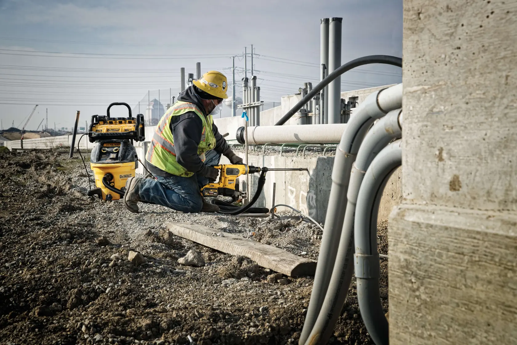 Photo of worker using DEWALT tool, SKUs DCH481X2, DCH481X2-GB, at construction site near pipes and conduit.