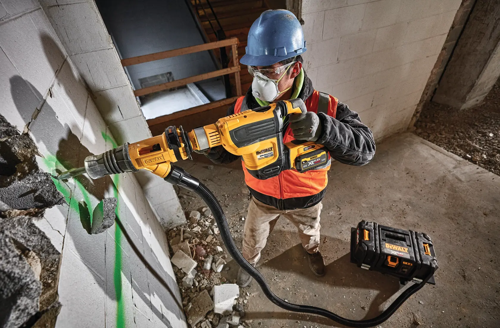 Worker using DEWALT rotary hammer drill with dust extraction on a concrete wall, wearing safety gear.