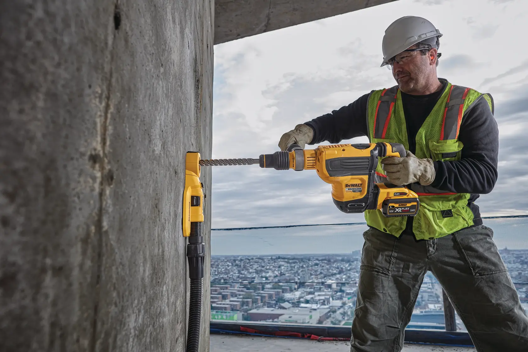 Worker uses DEWALT rotary hammer drill on a concrete wall at a construction site overlooking a cityscape.