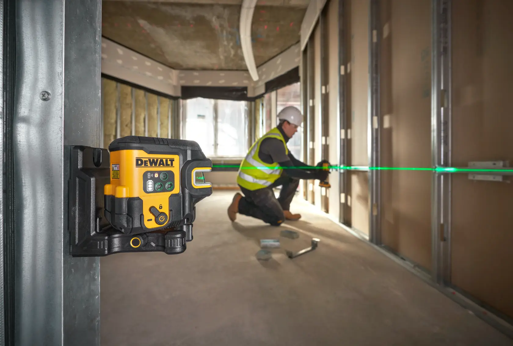 DEWALT laser level projecting a green line, used by a worker for aligning framing on a construction site.