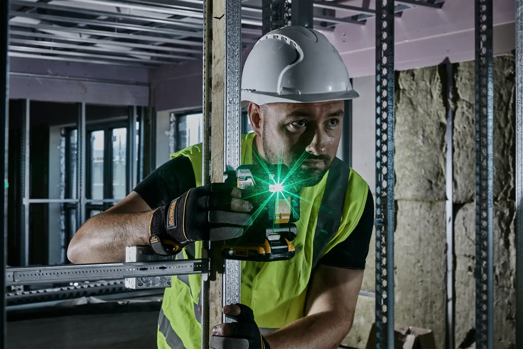DEWALT laser level used by a worker in safety gear for construction alignment inside a building.