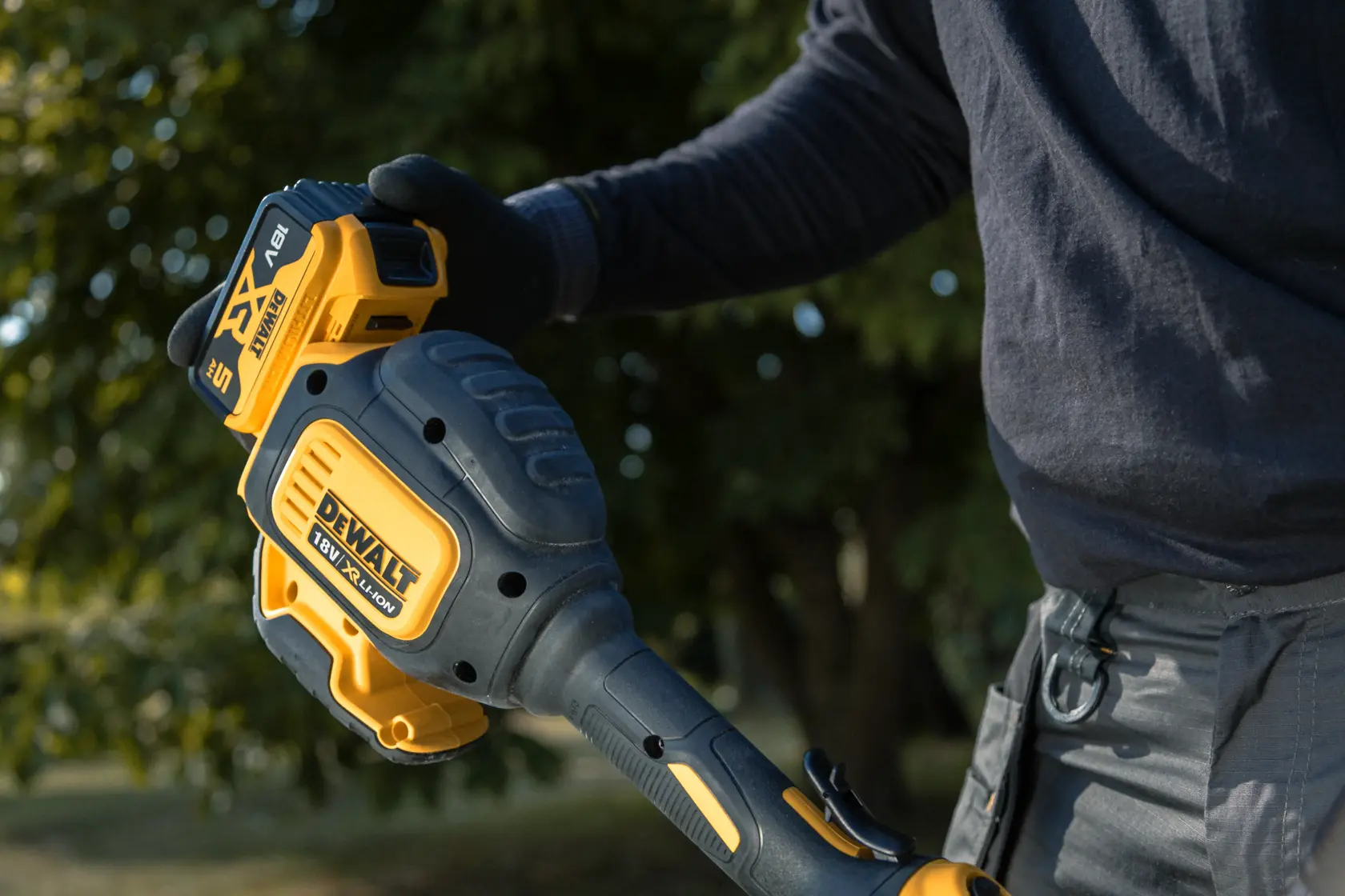 Person holding a DEWALT 18V cordless garden tool outdoors, close-up view of grip and battery area.