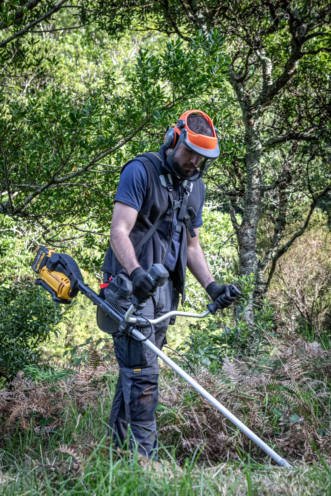 Person mit DEWALT Rasentrimmer, DCMST922N, DCMST922N-XJ, draußen mit Schutzausrüstung.