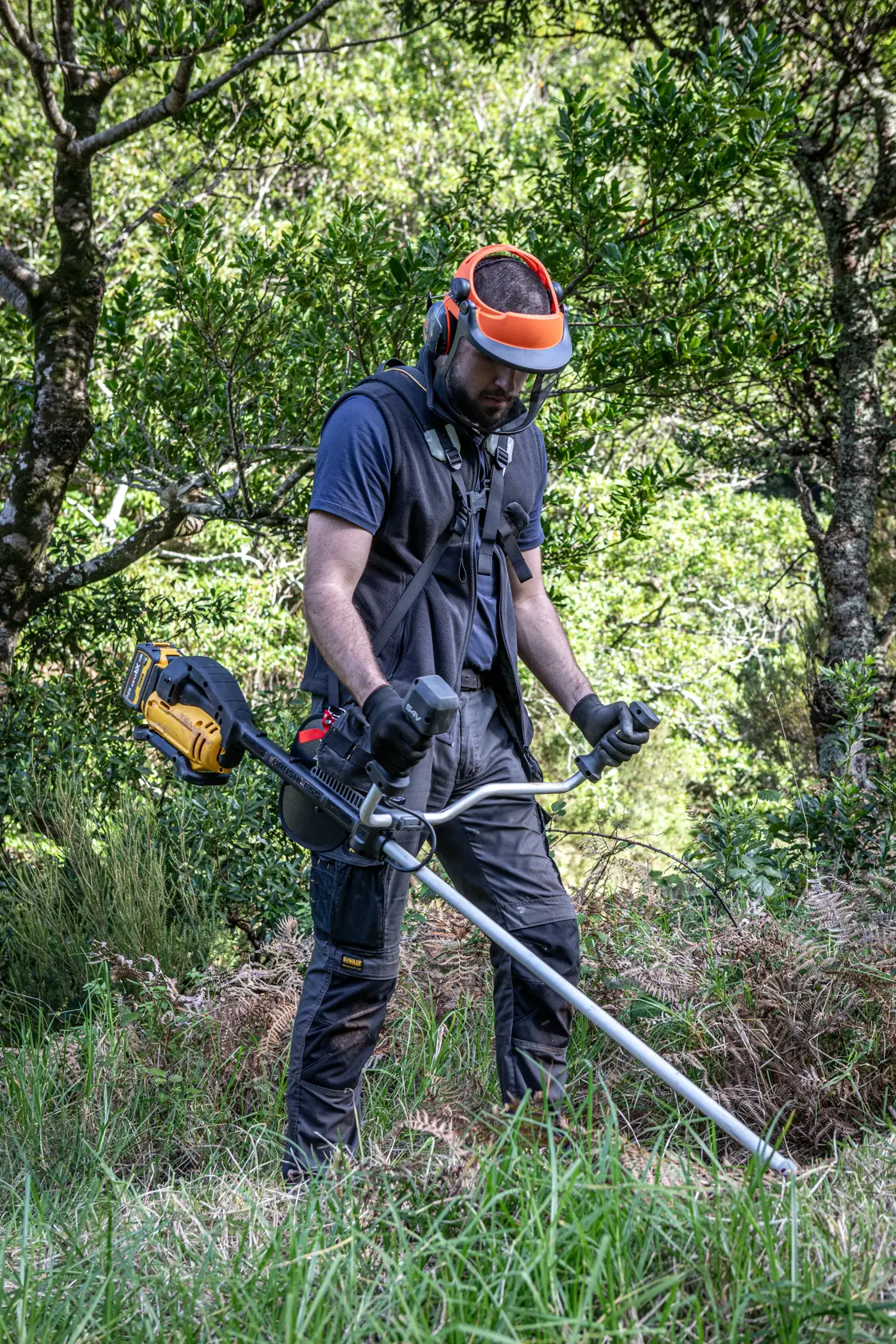 Person mit DEWALT DCMST922N, DCMST922N-XJ Freischneider und Schutzkleidung im Grünen.