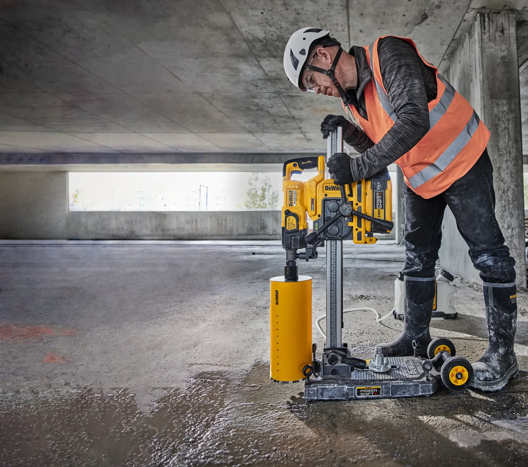Image montrant le stand de perceuse à carottage DEWALT DCPS151 Powershift avec une perceuse jaune et noire montée verticalement sur un rail métallique avec des roues. Le produit comprend divers accessoires comme un levier d'alimentation, un connecteur de tuyau d'aspirateur, un écrou de serrage, une tige filetée, un outil de réglage et des pièces drop-in. Une liste des éléments inclus est présentée dans une section noire et jaune en haut.