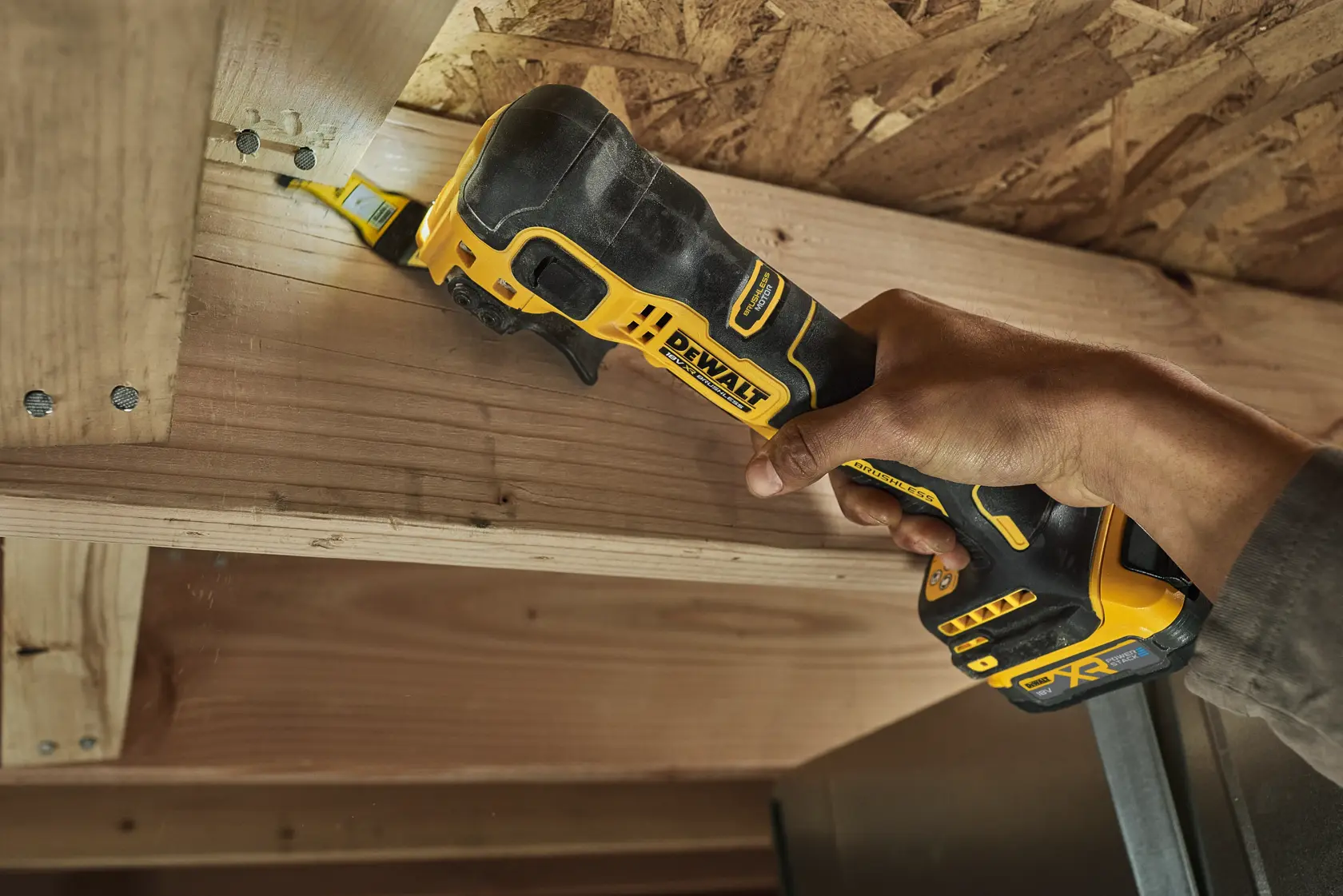 A hand using a DEWALT DCS358 oscillating multi-tool to cut wood in a tight space.