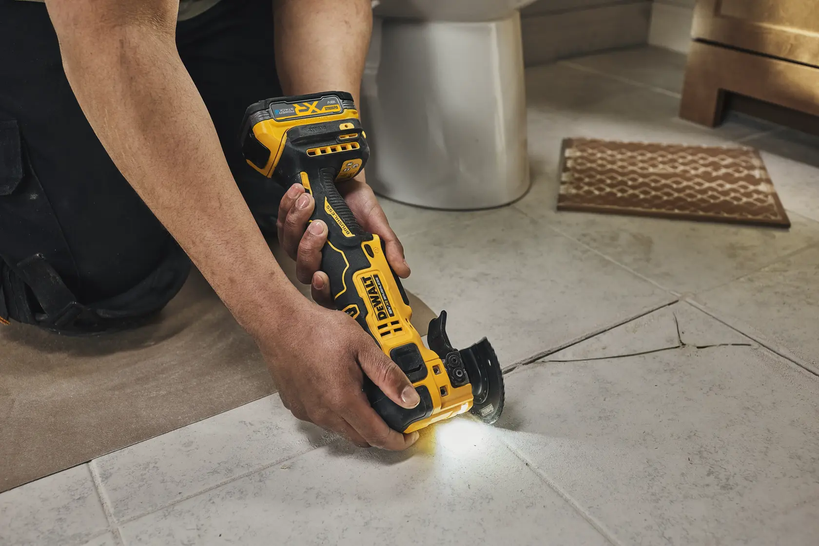 Person using a DEWALT cordless multi-tool to cut tiles on a floor, with built-in light illuminating the work area.