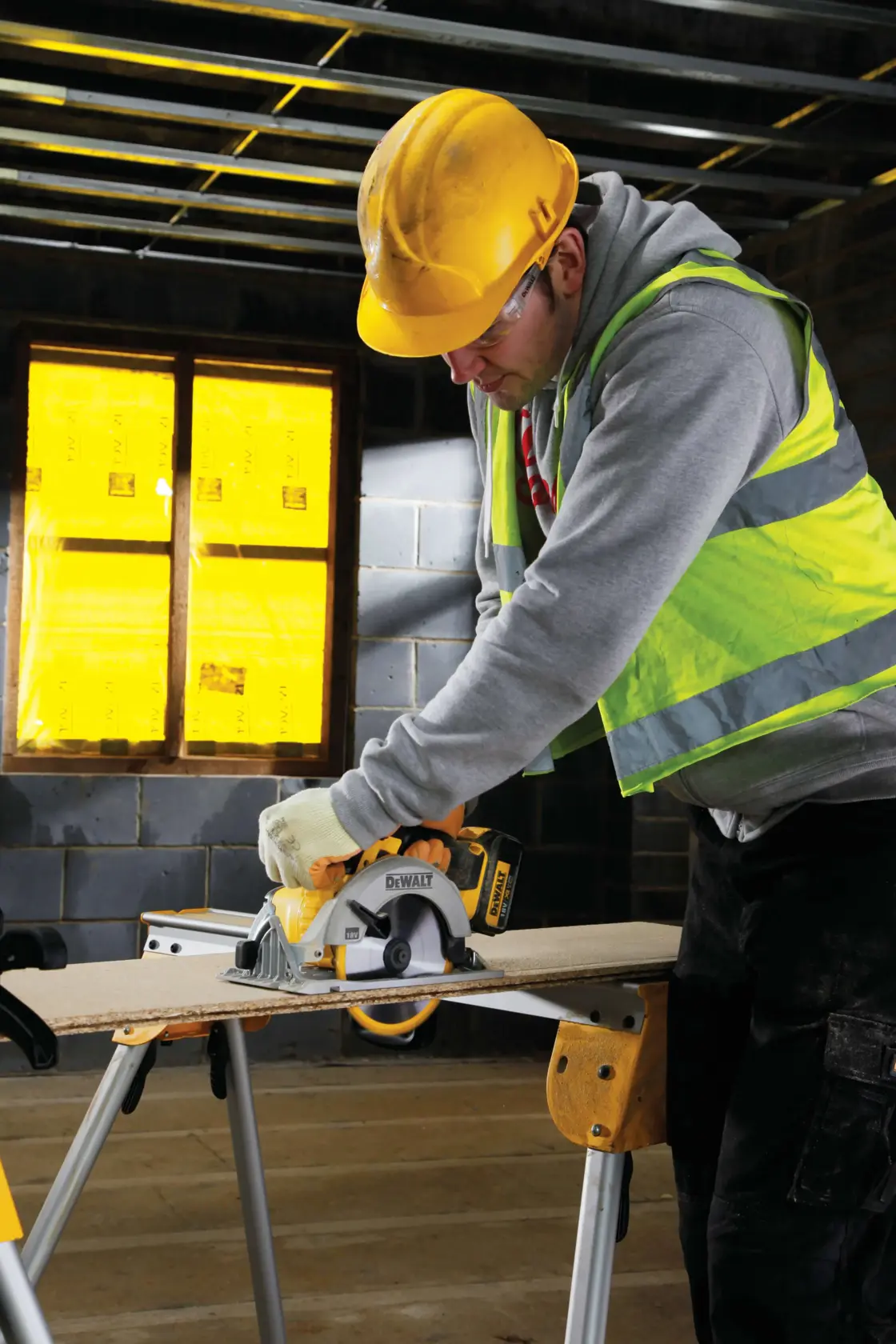 Worker uses a DEWALT circular saw to cut wood on a sawhorse in a construction site.