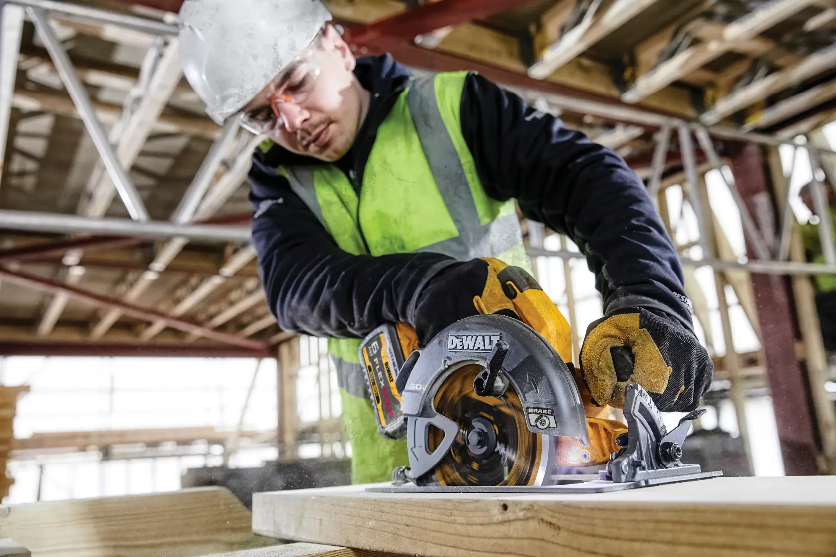 Worker uses a DEWALT DCS578T2 circular saw to cut wood on a construction site, wearing safety gear and gloves.