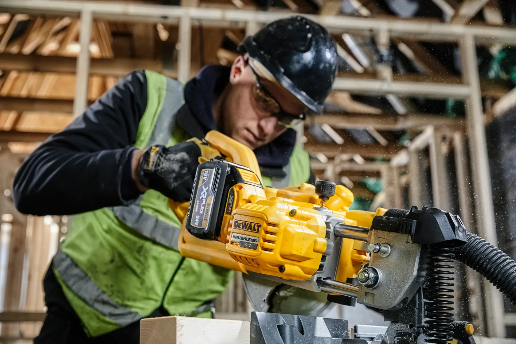 Worker using a DEWALT cordless saw DCS777T2 in a wooden construction area, wearing safety gear and vest.