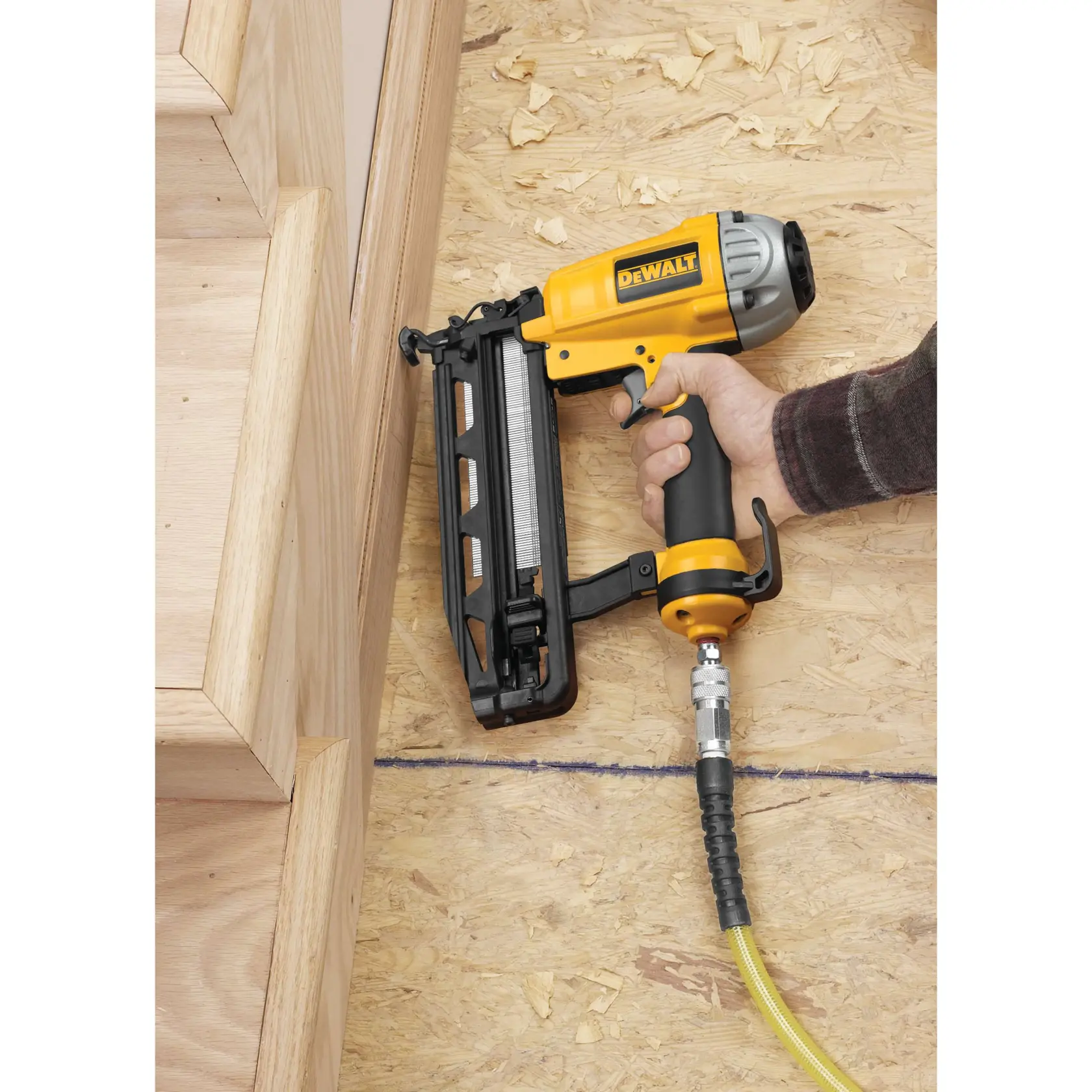 A DEWALT pneumatic nailer is being used to install wooden stair trim on a plywood floor.