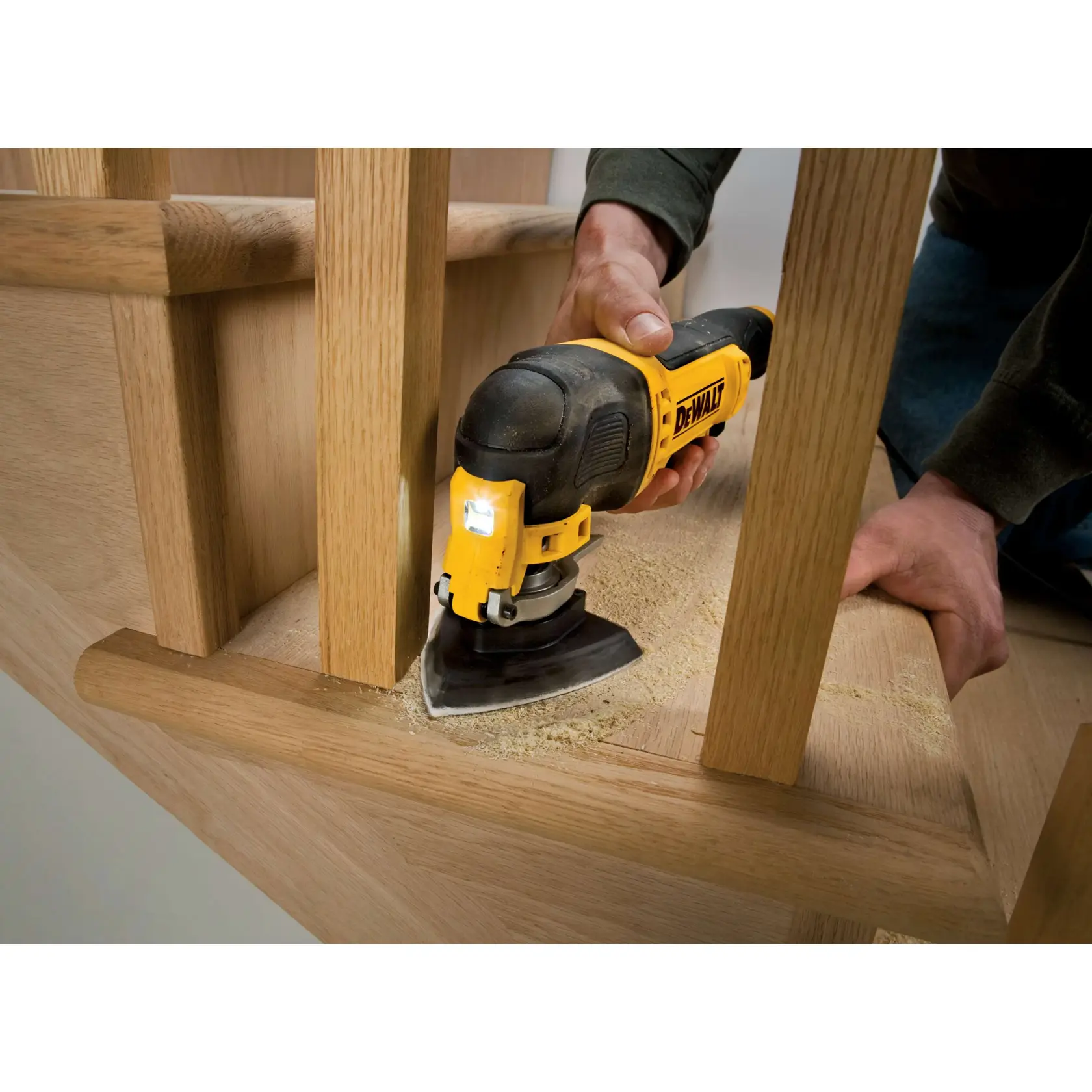 DEWALT multitool sanding wood on staircase. Sawdust visible. Person holding tool, close-up of working area.