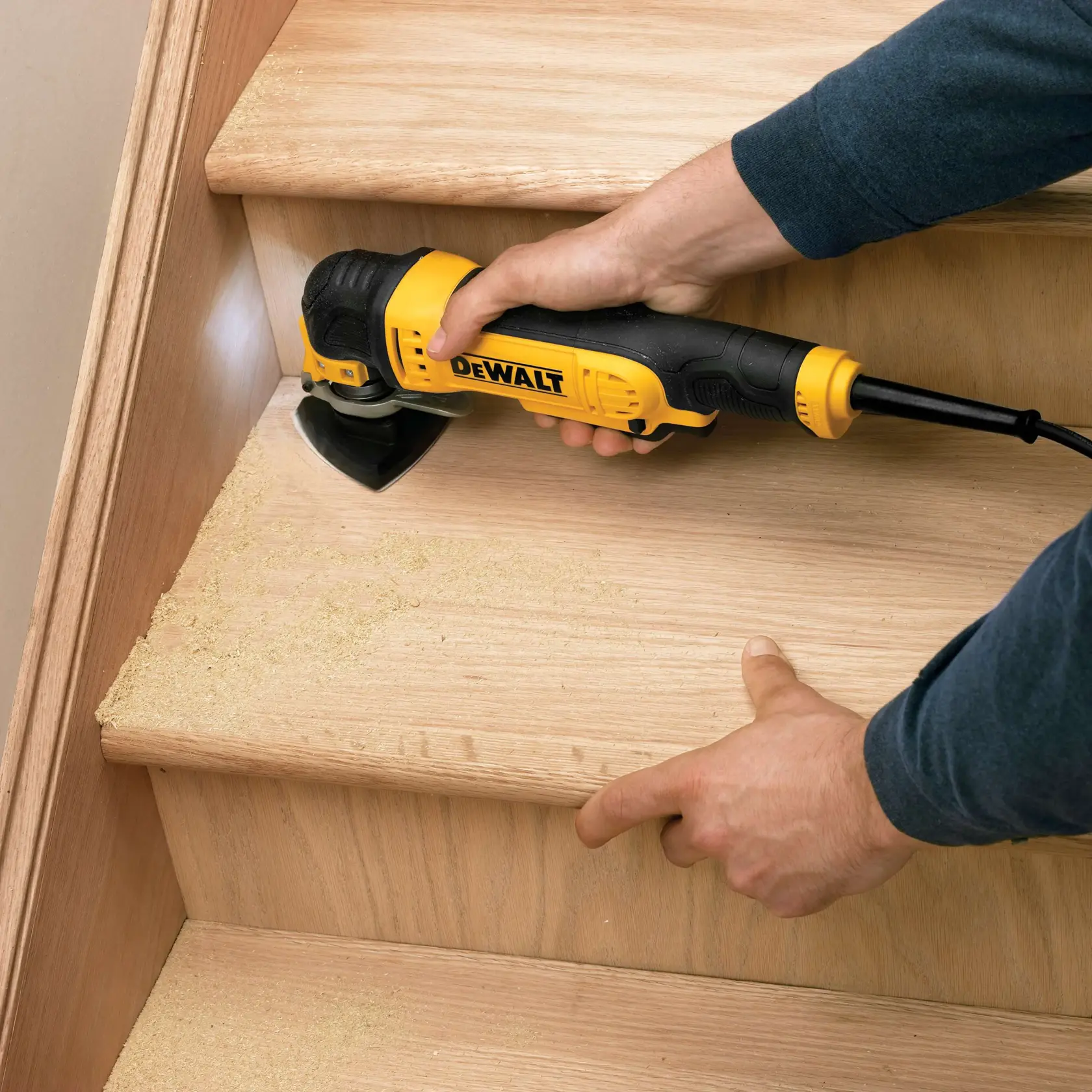 A DEWALT tool is used to sand wooden stairs, creating sawdust. Hands hold and operate the sander on a stair step.