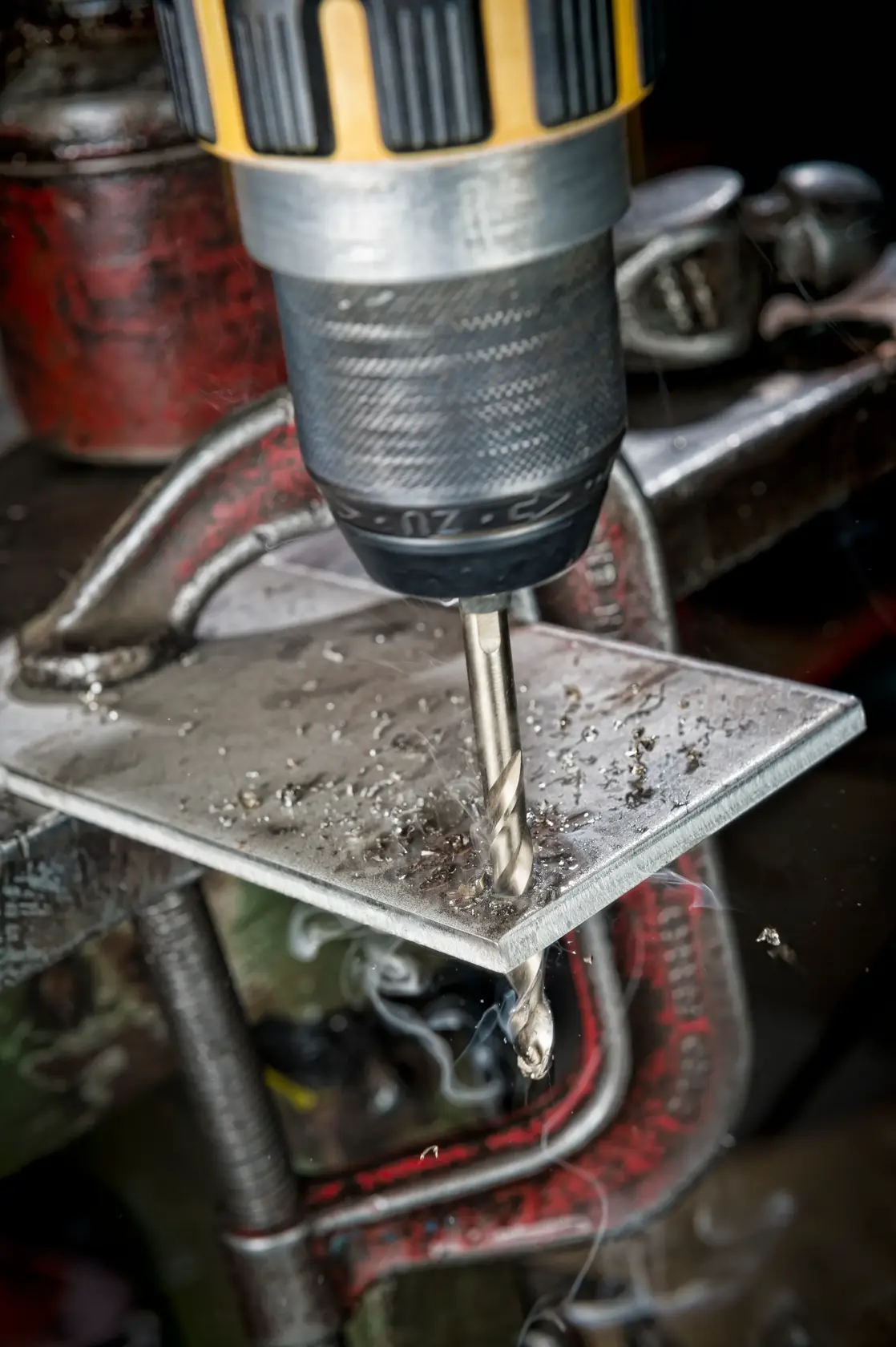 Close-up of a DEWALT drill bit drilling into a metal plate, metal shavings visible around the area.