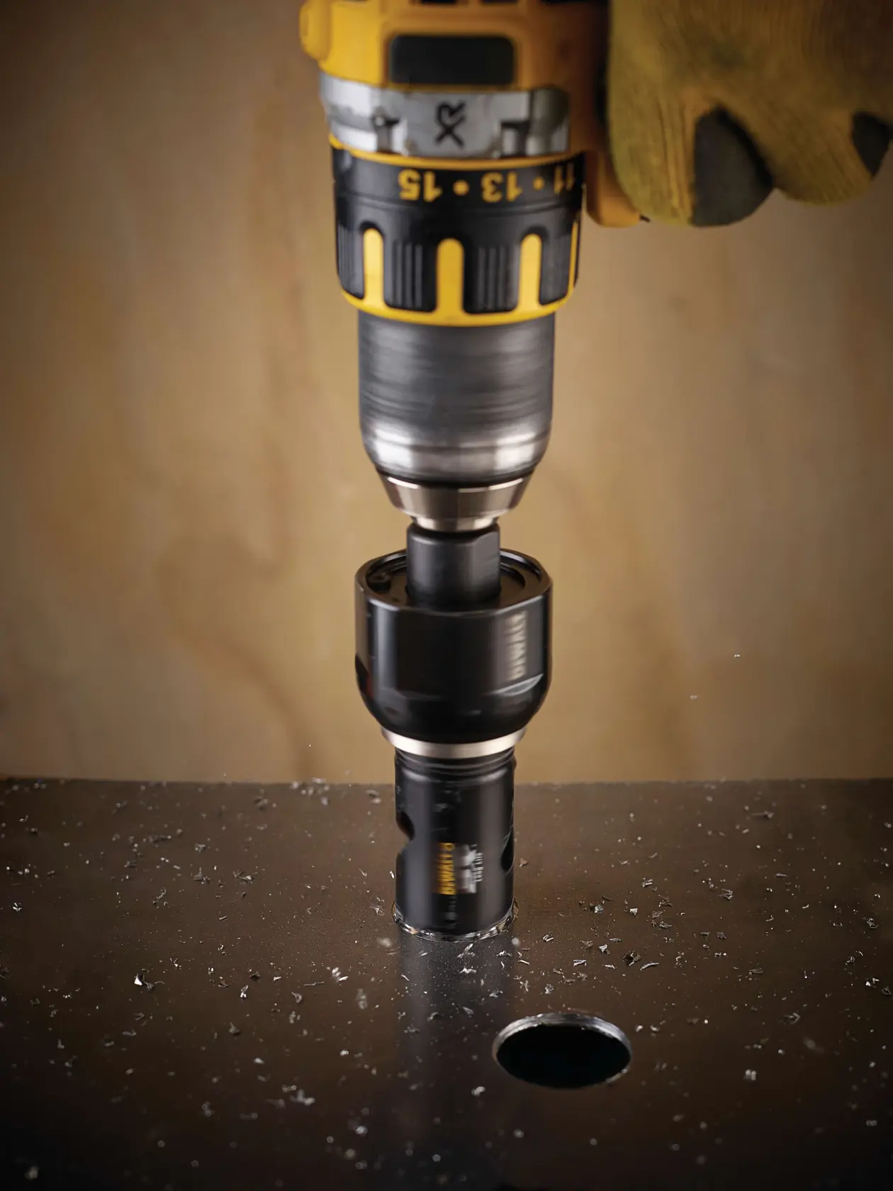 DEWALT drill with DT8124L hole saw cutting a circular hole in a metal sheet, worker uses protective glove.