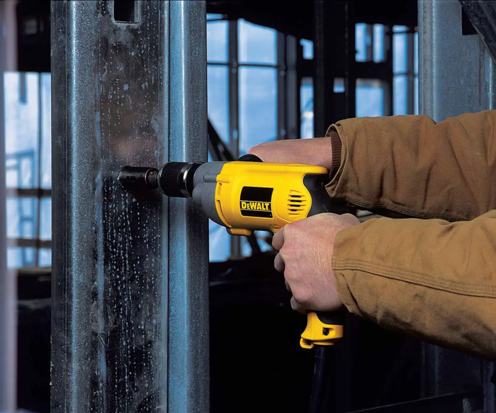 Person using a yellow DEWALT drill to work on a metal beam indoors.