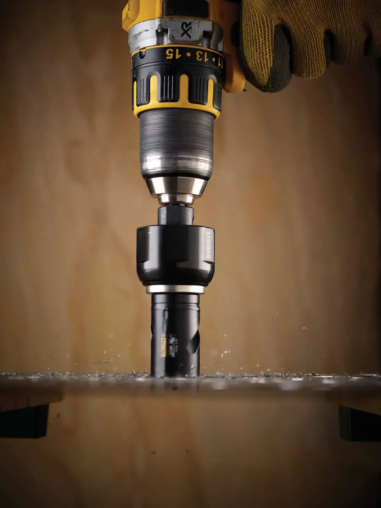 DEWALT drill with hole saw cutting through a flat metal surface, operated by a gloved hand.