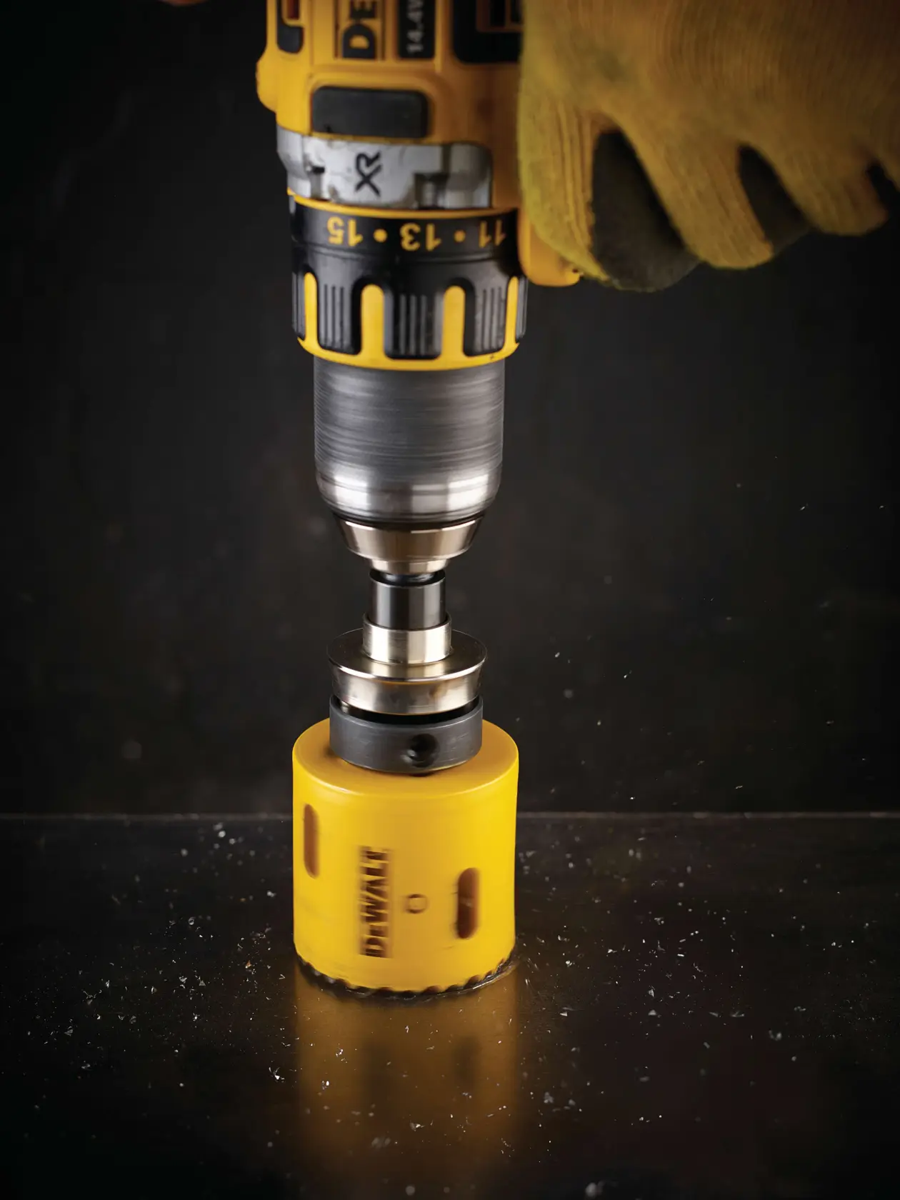 DEWALT drill with yellow hole saw cutting into metal surface, operated by a gloved hand.