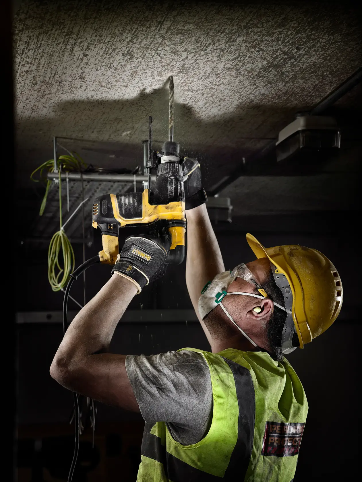 Trabajador perfora techo con herramienta DEWALT, lleva casco, chaleco, guantes y mascarilla.